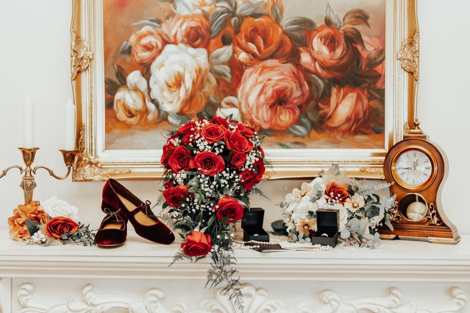 Red rose bouquet on white mantel with vintage clock, painting, and decorative shoes.