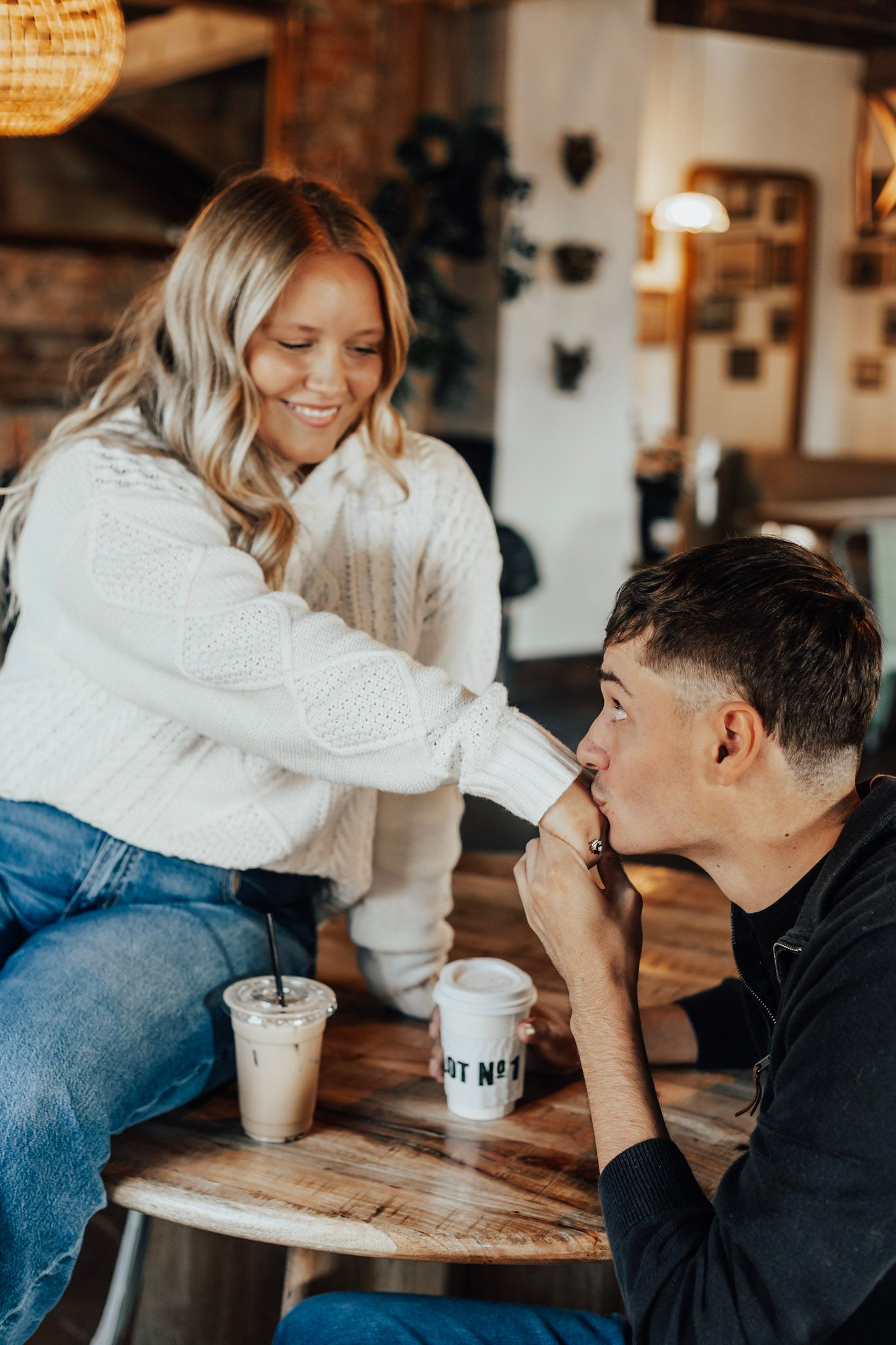 Playful interaction between two people at a wooden table with drinks.