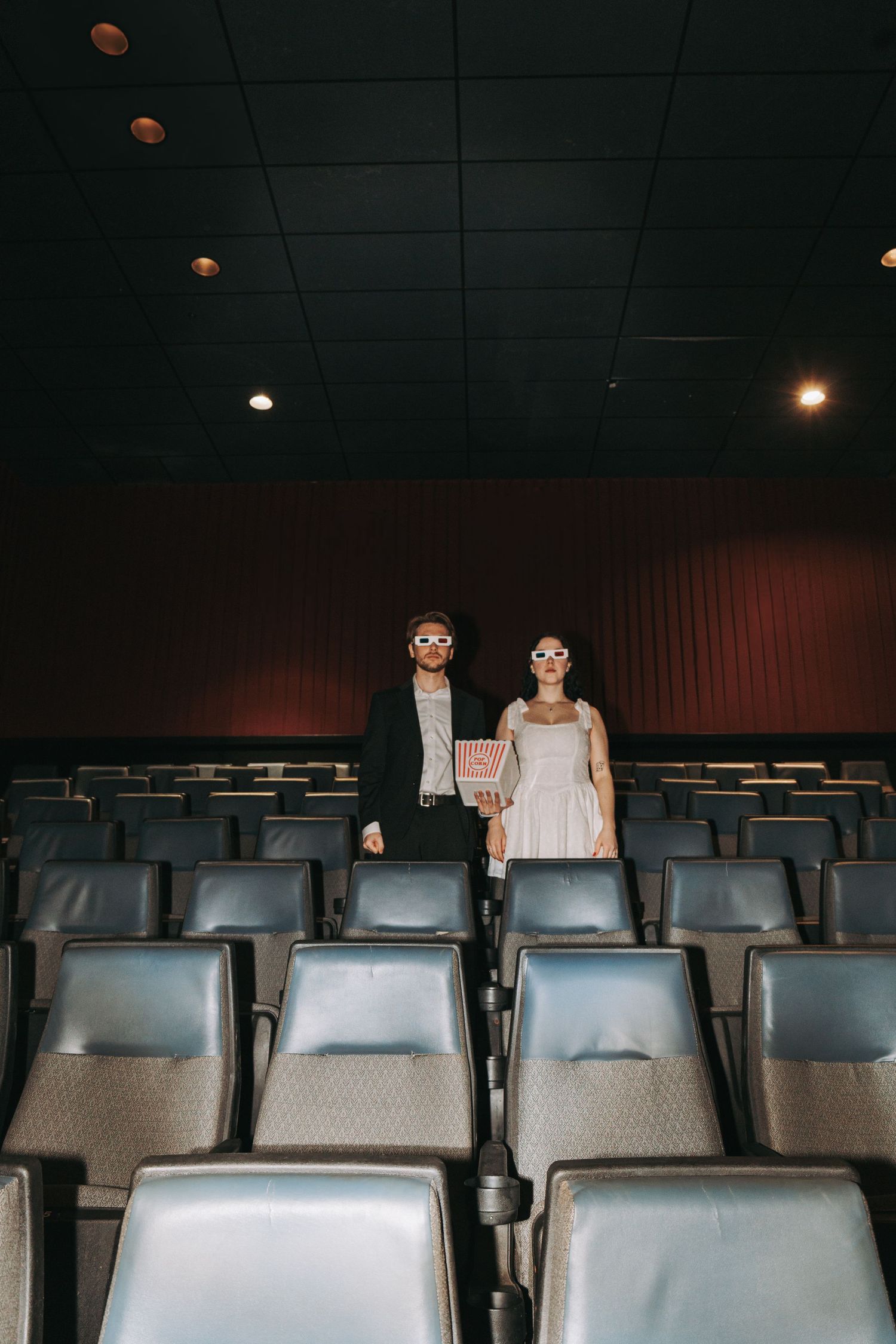 A dark movie theater with rows of empty blue seats and dim lighting overhead.