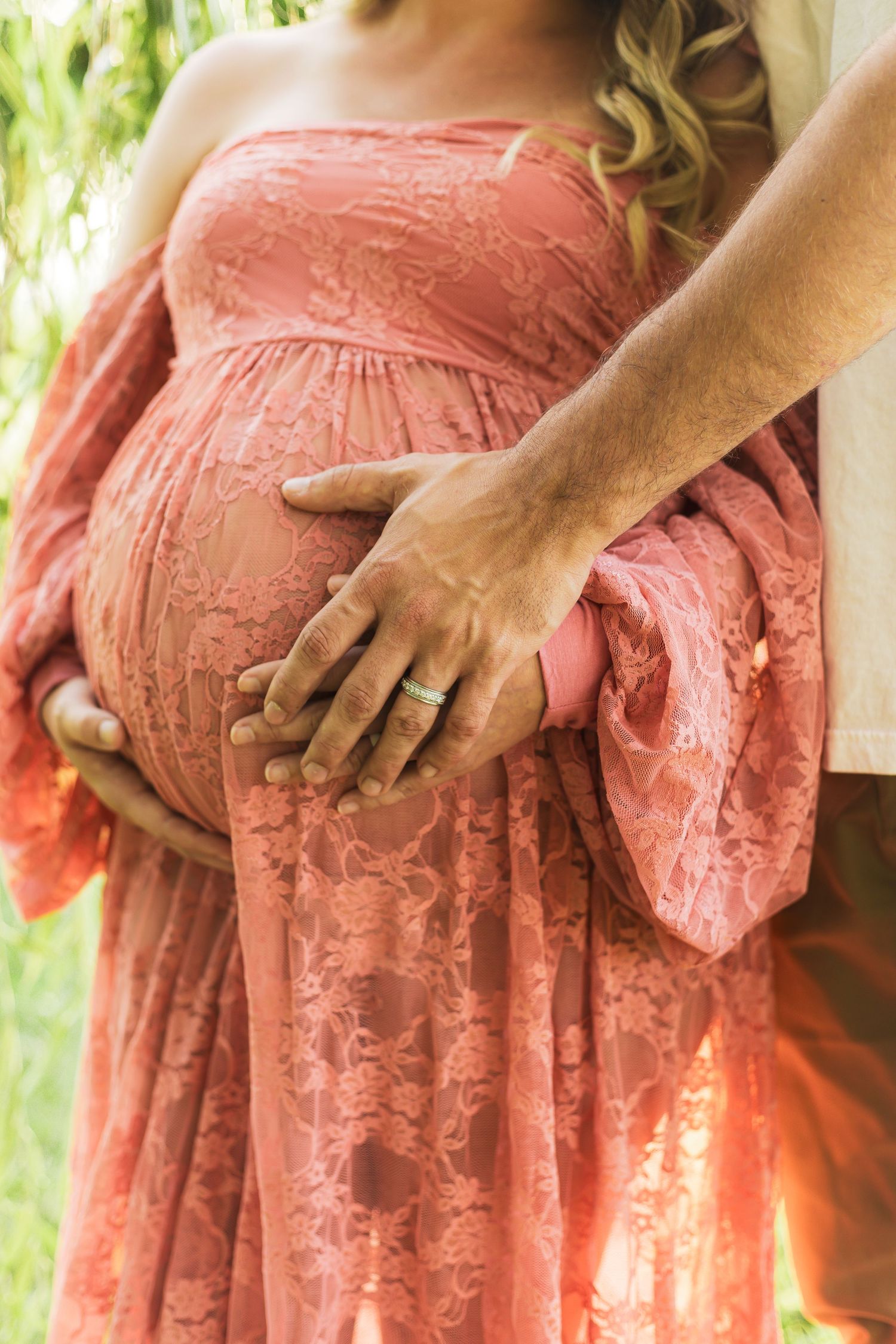 Close-up details of a coral lace maternity dress showing the delicate fabric and baby bump.