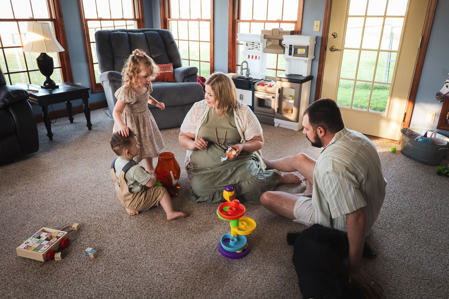 Family playtime on a carpeted floor with colorful toys scattered around.