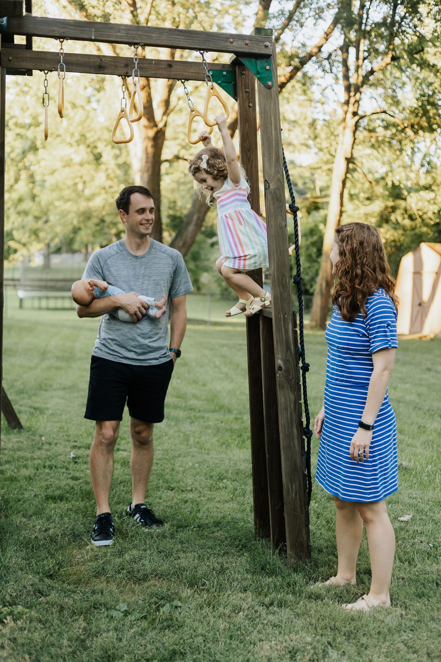 Family playing together on outdoor playground equipment in a grassy backyard.