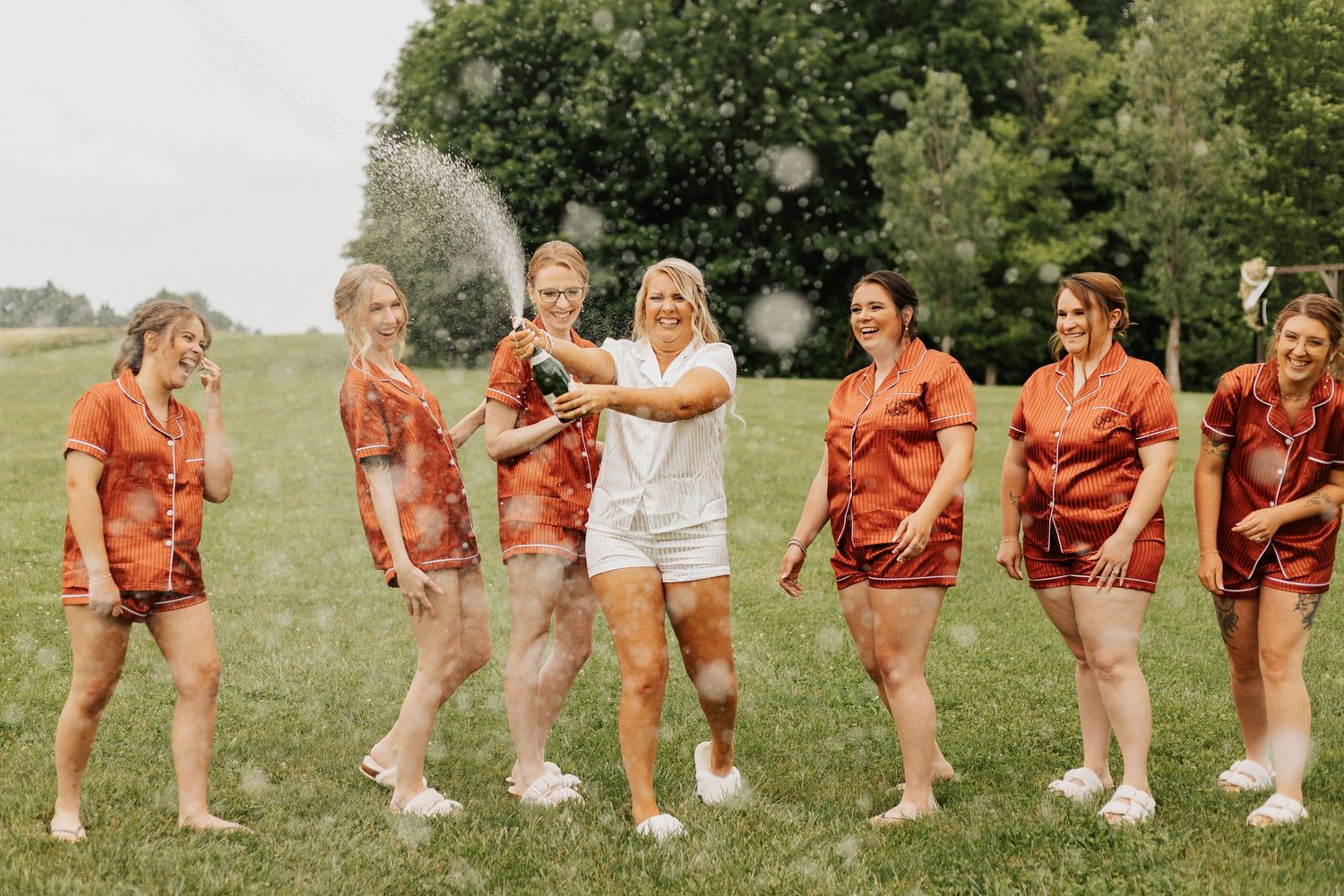 Wedding party in red outfits performs choreographed dance moves on grass.