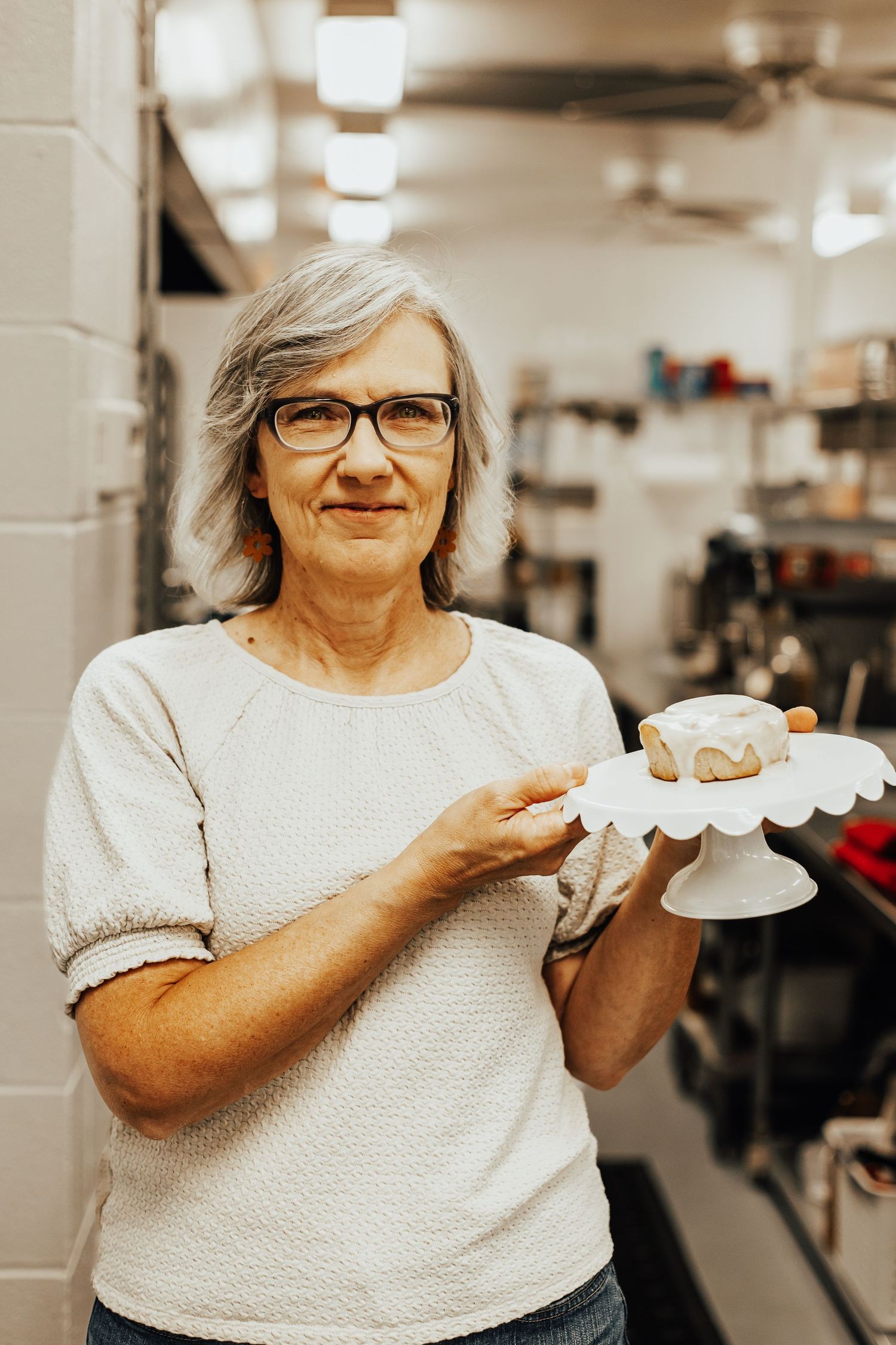 Baker presenting freshly baked goods on white serving plates in commercial kitchen.