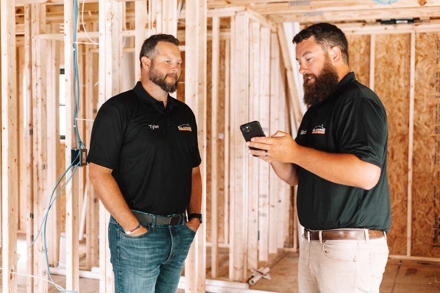 Construction worker in black polo shirt examining interior framing of new building project.