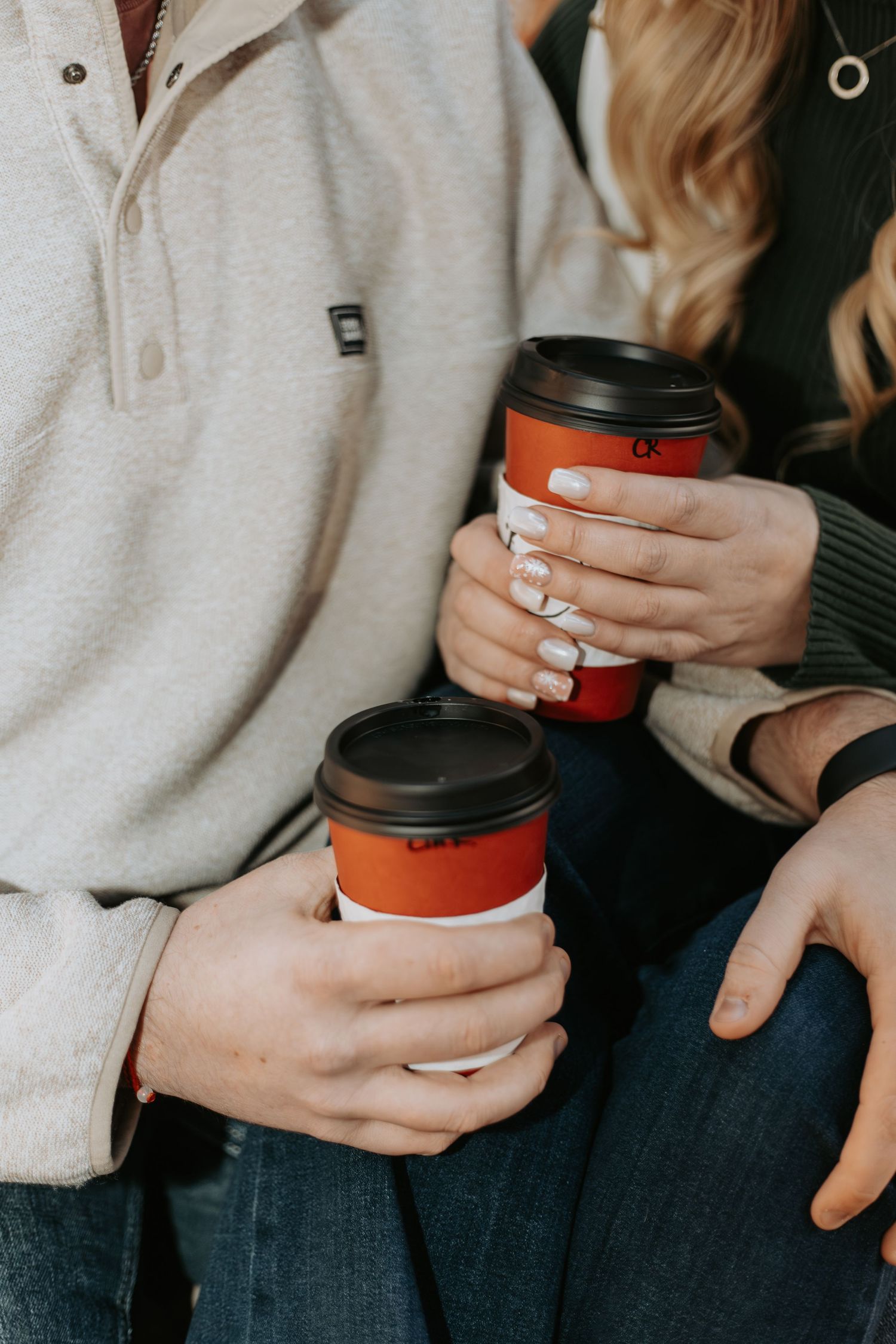Close-up of hands holding red coffee cups while wearing coordinating winter outfits.
