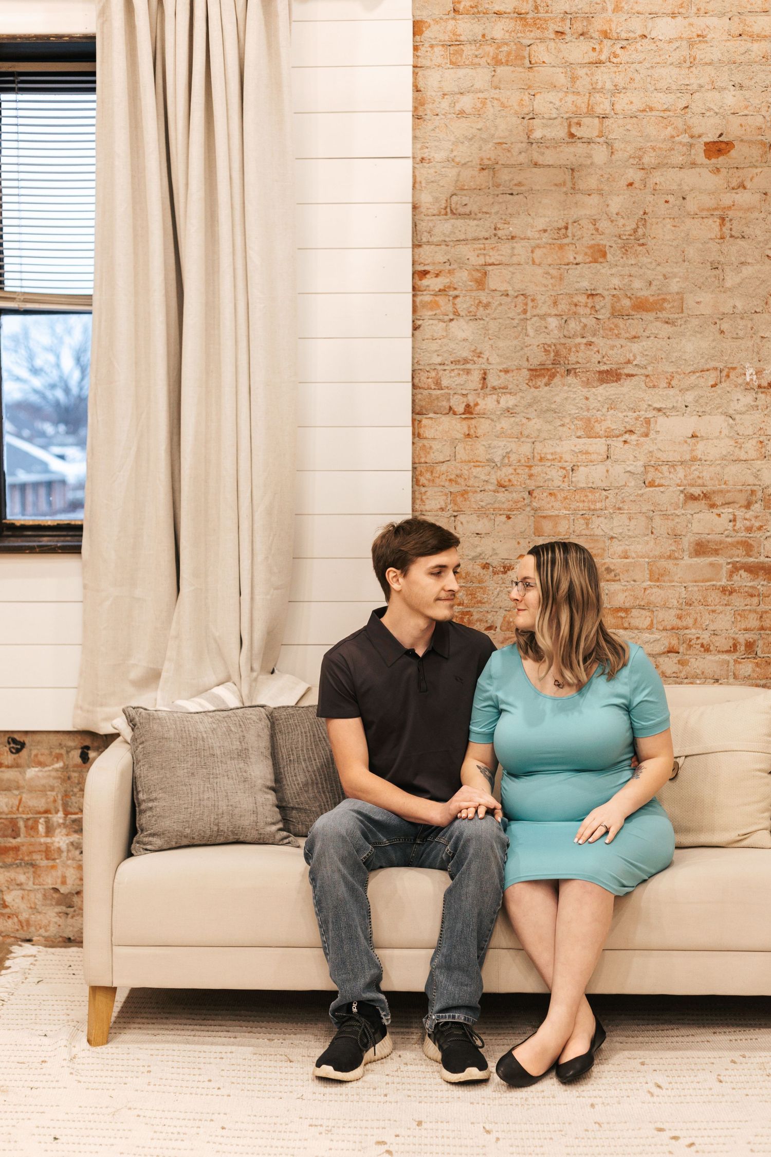 Couple sitting together on a white couch against exposed brick wall in an industrial-style room.
