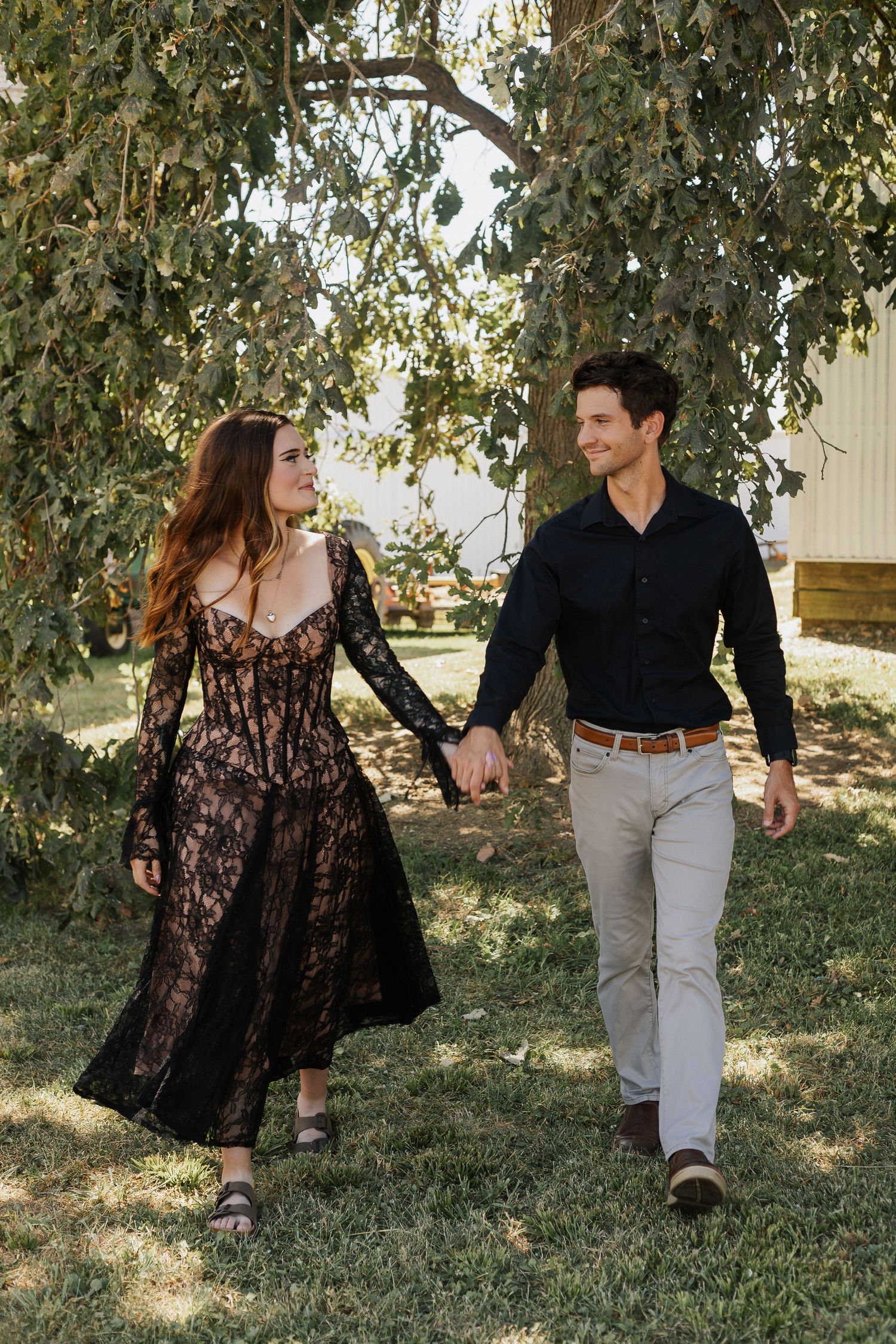 Couple walking together outdoors in a garden setting with trees in the background.