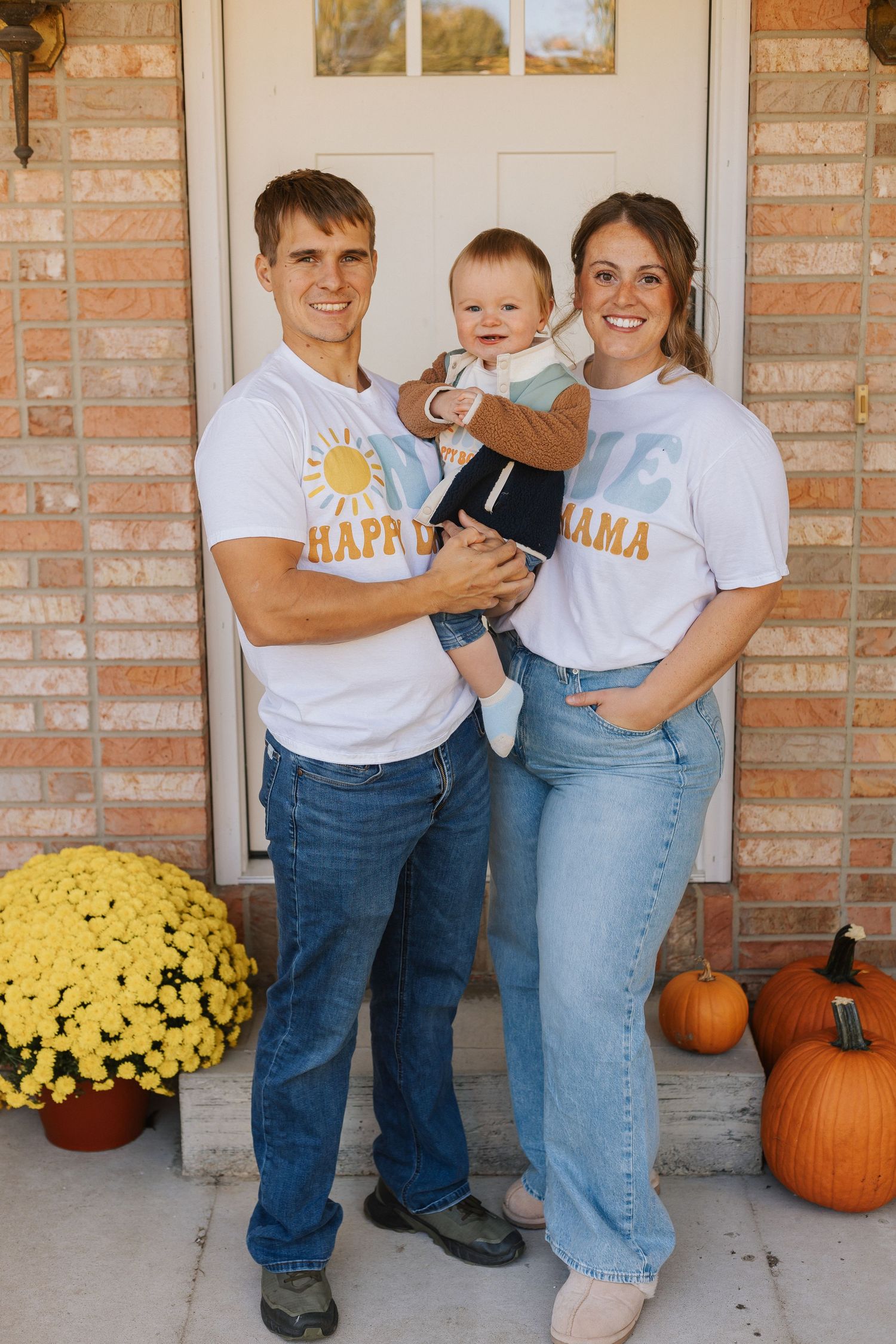 Fall themed family photo with pumpkins and yellow mums on brick porch.