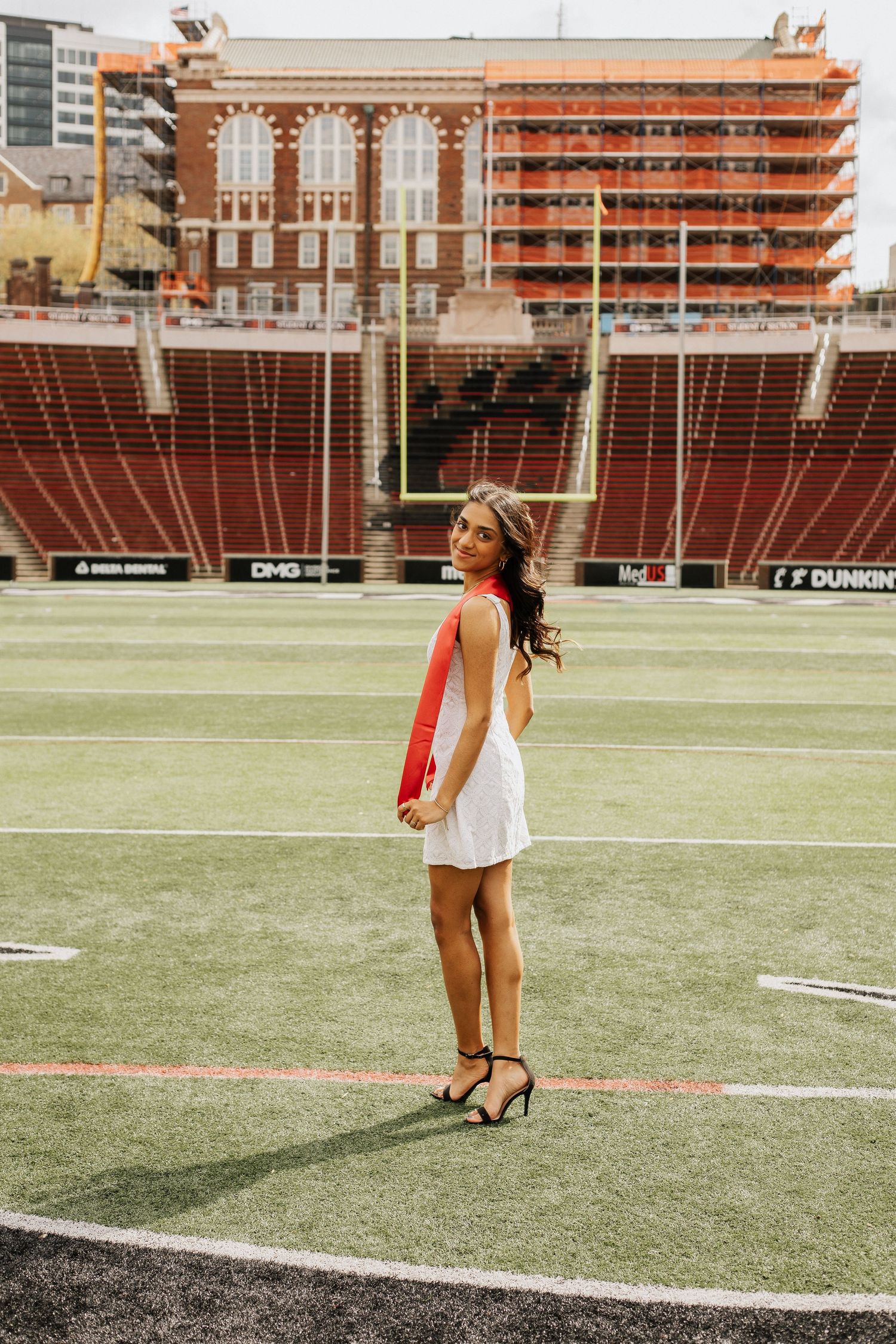 White dress against football field backdrop with stadium seating and architecture.