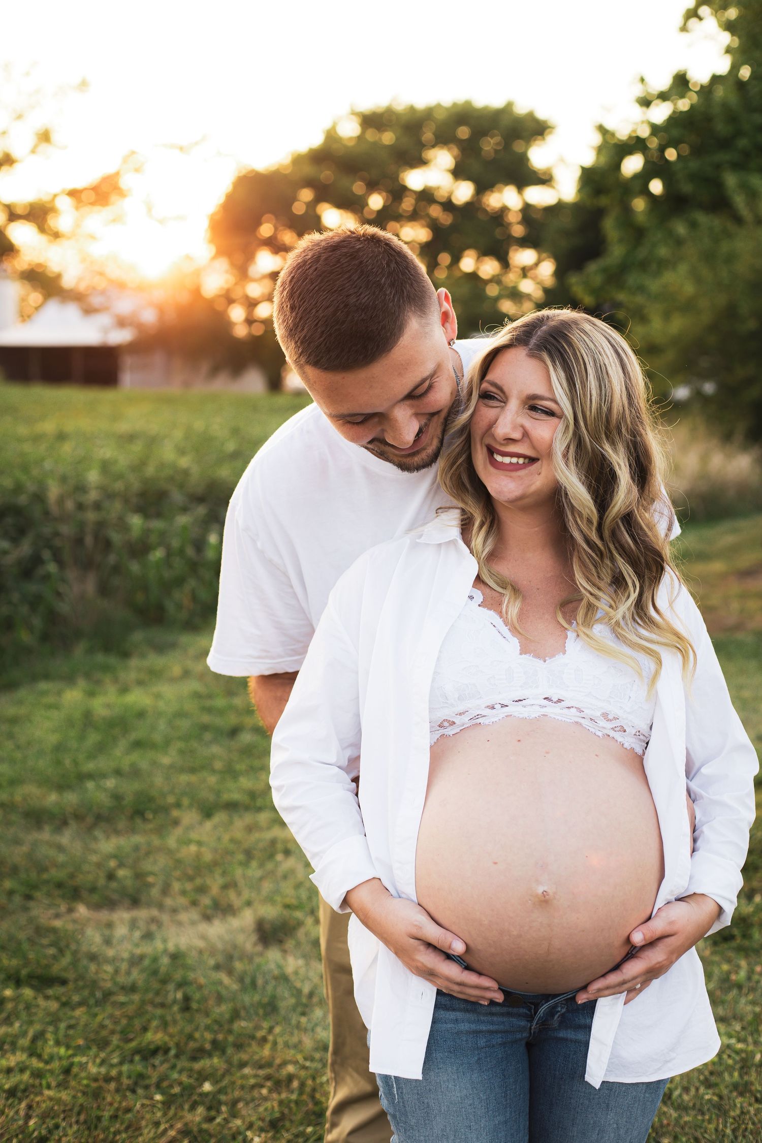 Sunset maternity photos showing joyful moments between expecting couple in casual attire.
