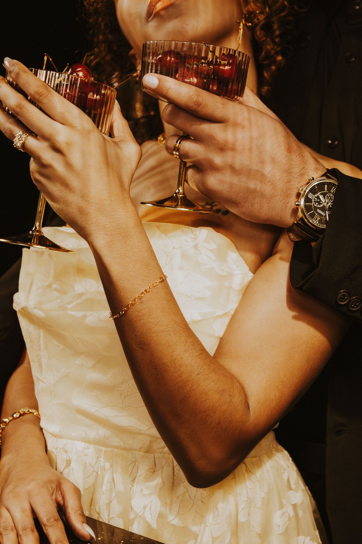 Hands adorned with jewelry holding a wine glass in a white dress.