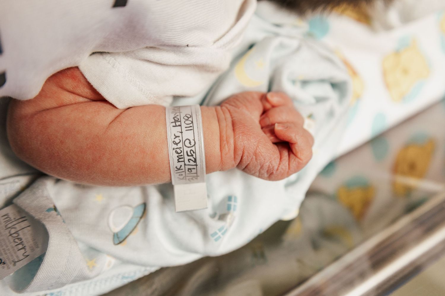 Close-up of medical staff hands holding and checking newborn baby identification bracelet in hospital.