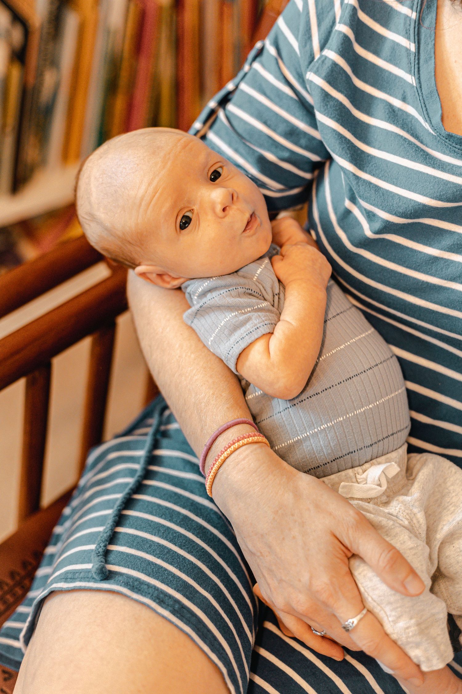 Baby in grey outfit being held in striped shirt.