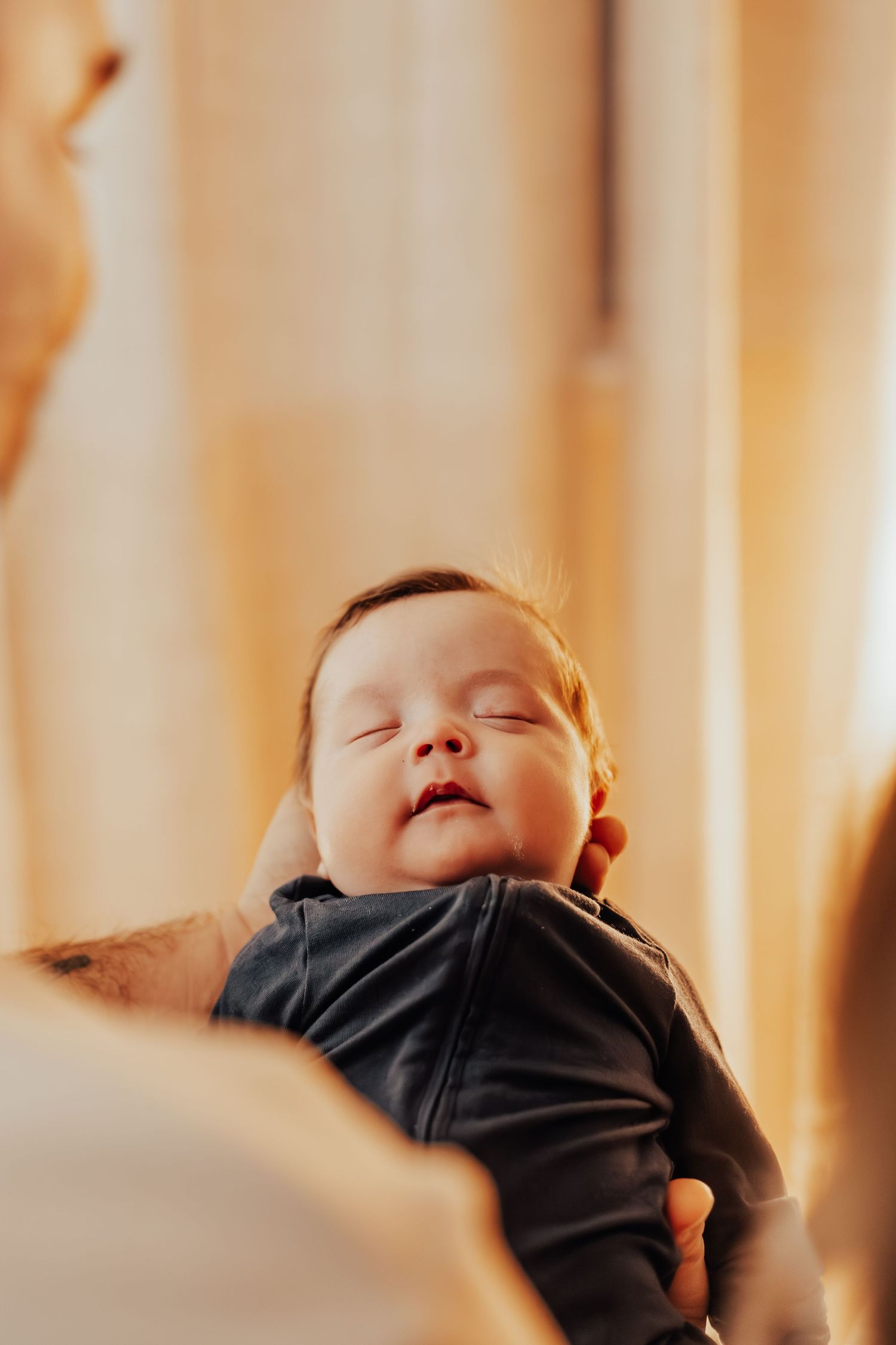 Close-up of a sleeping infant in dark clothing against soft window light.