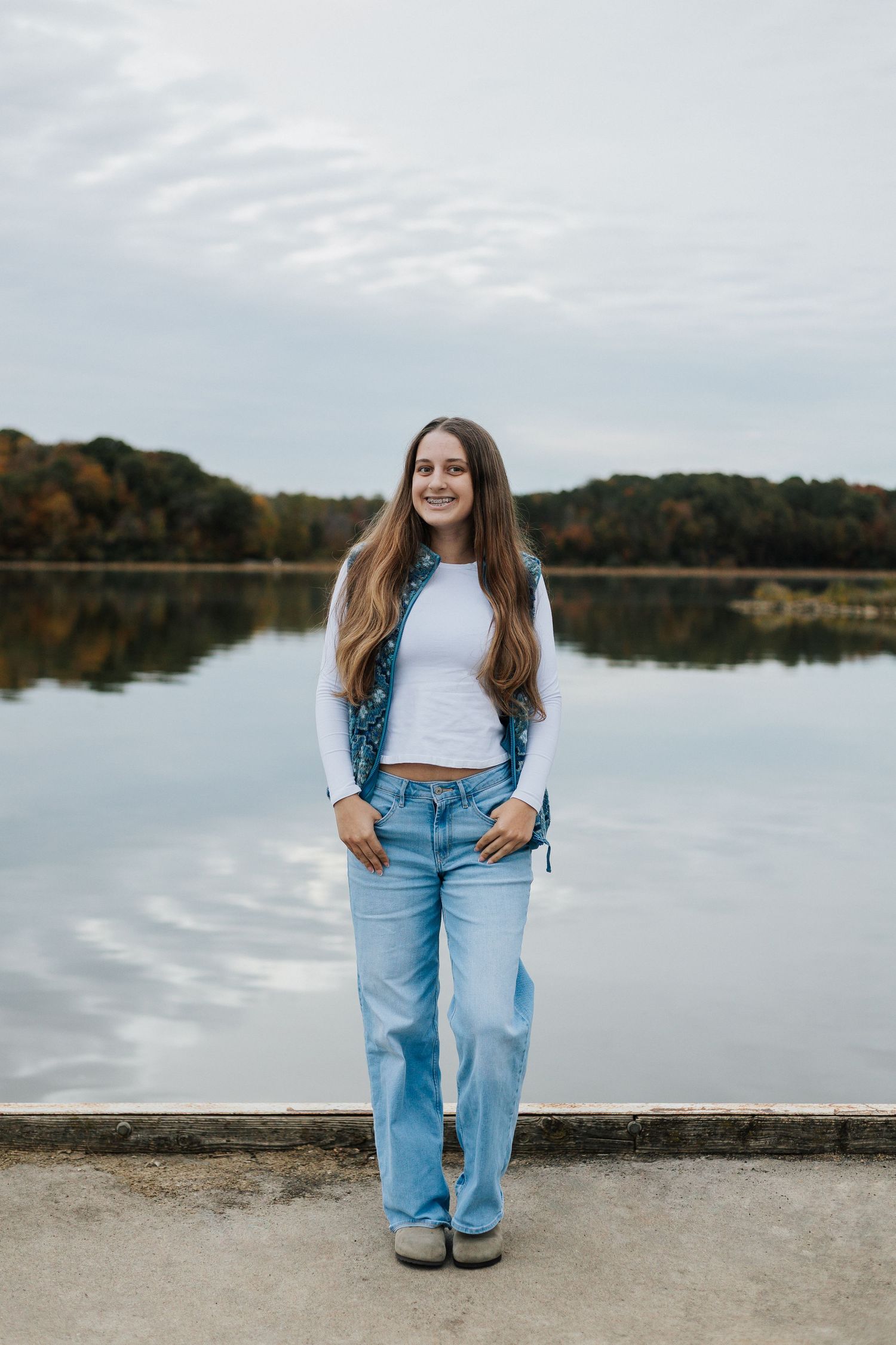 Casual portrait session by serene lake with autumn trees reflecting in still water.