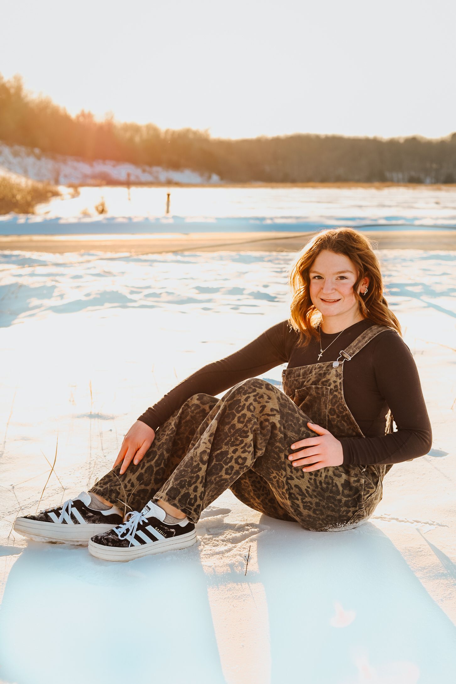 Winter portrait session with someone lounging in the snow at sunset wearing casual attire.
