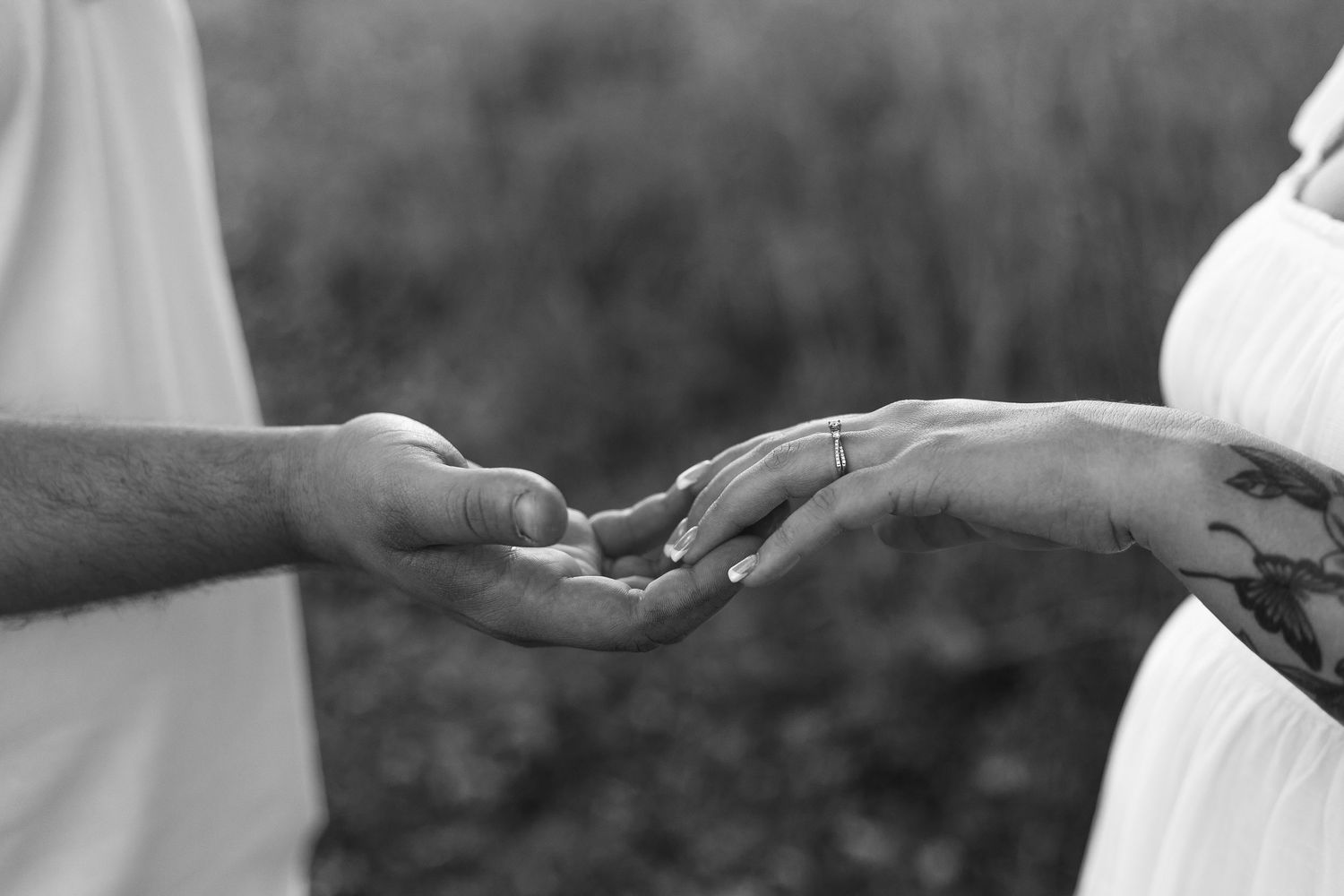 Black and white close-up of hands exchanging a ring during a romantic moment.
