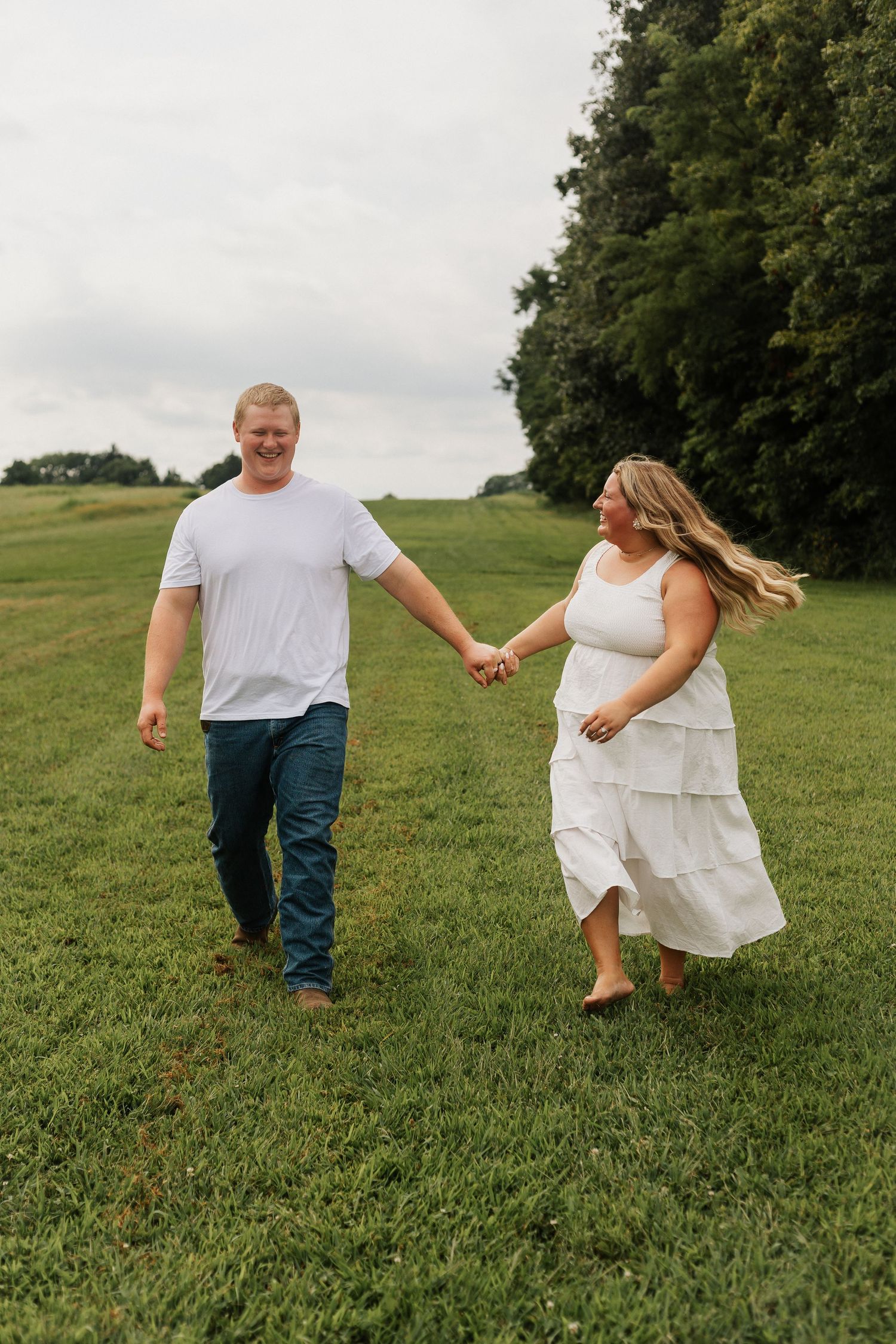 A couple holds hands while walking playfully through a grassy field.
