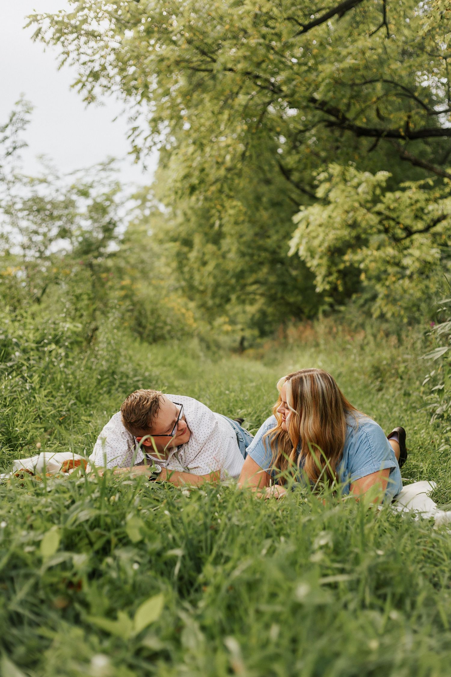 Couple lying on white blanket in green meadow during summer photoshoot.