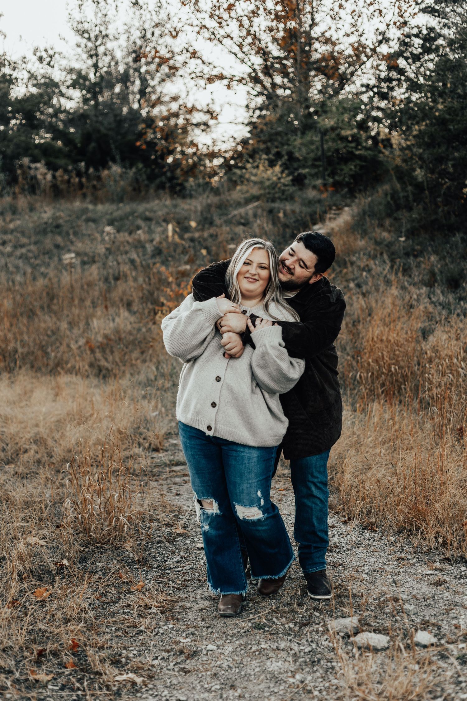 Couple sharing playful moment on dirt path surrounded by autumn foliage.
