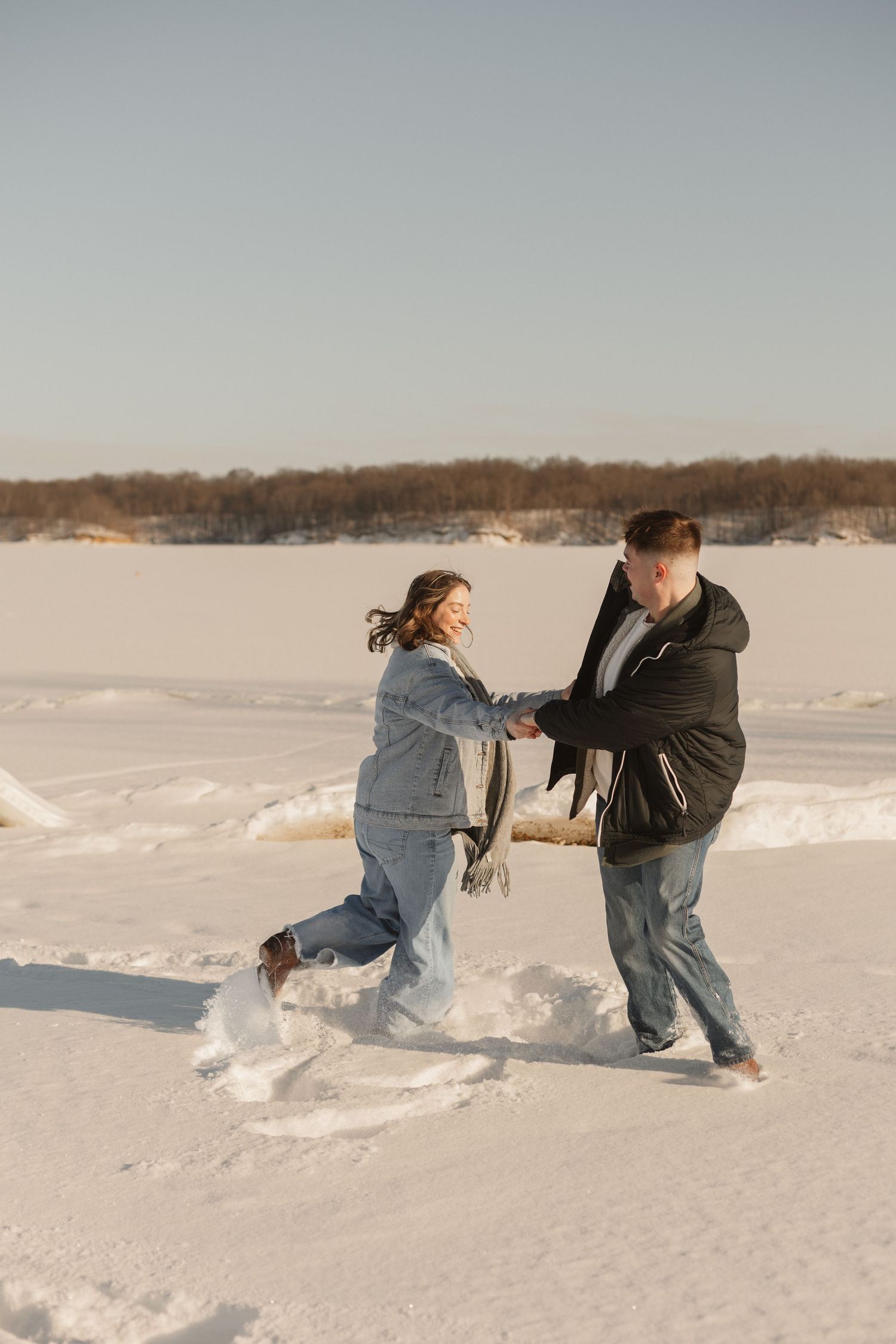 A couple plays in the snow during a winter engagement photoshoot.