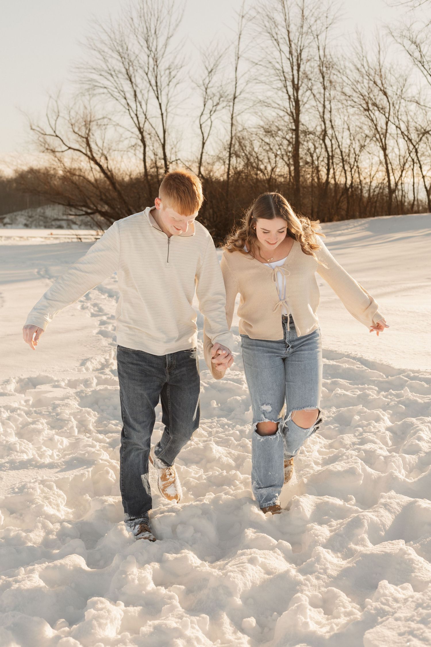 A couple walks hand in hand through deep snow during a winter photoshoot.