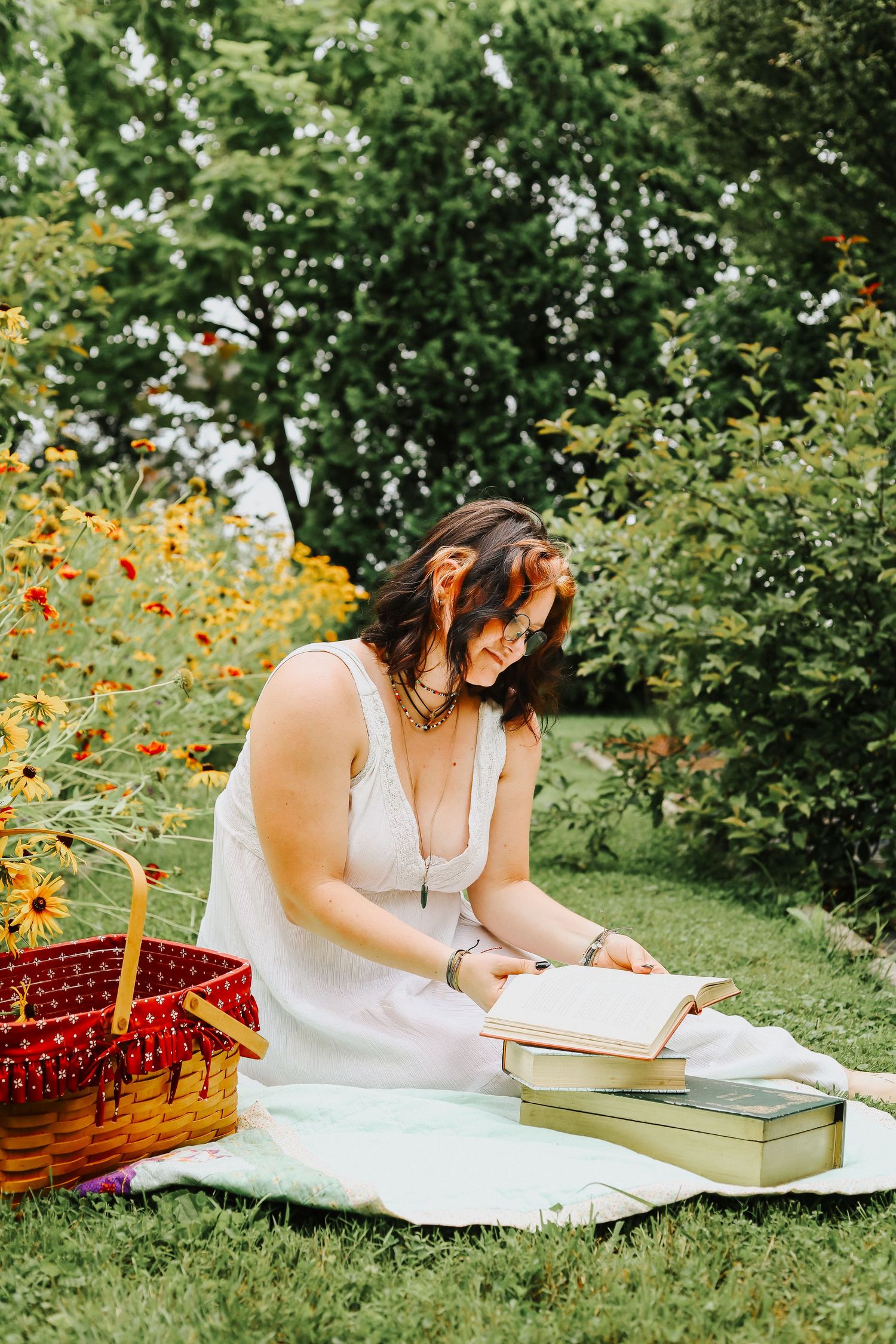 A peaceful garden scene with someone in white reading beside a picnic basket among flowers.