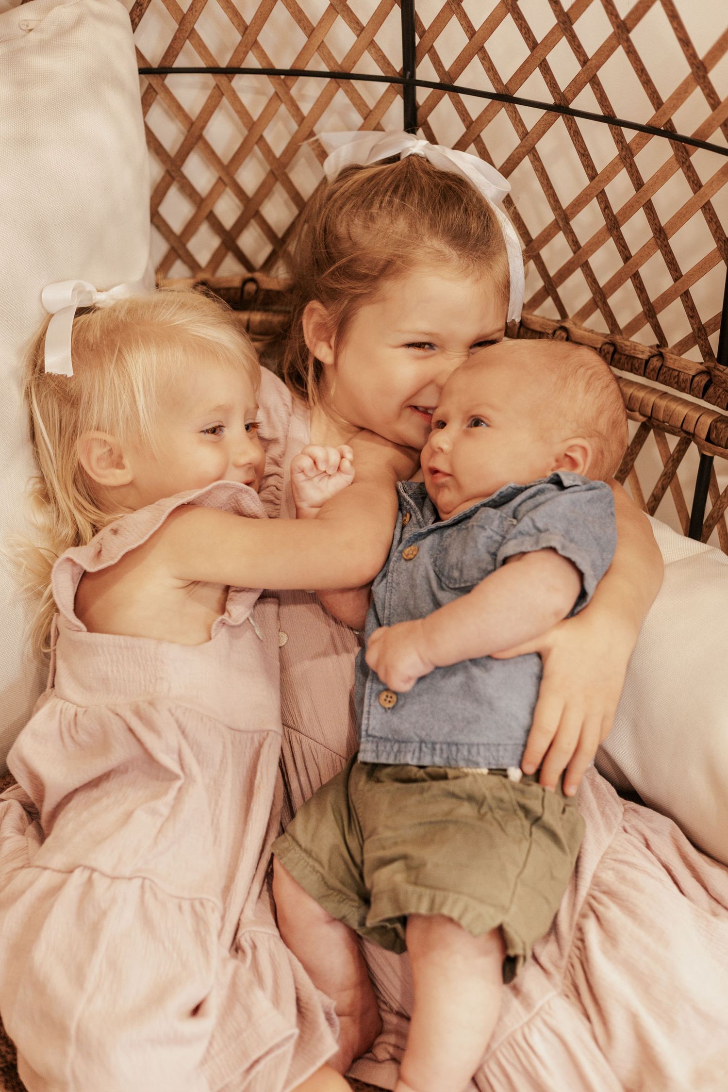 Three children cuddling and laughing together in wicker chair.