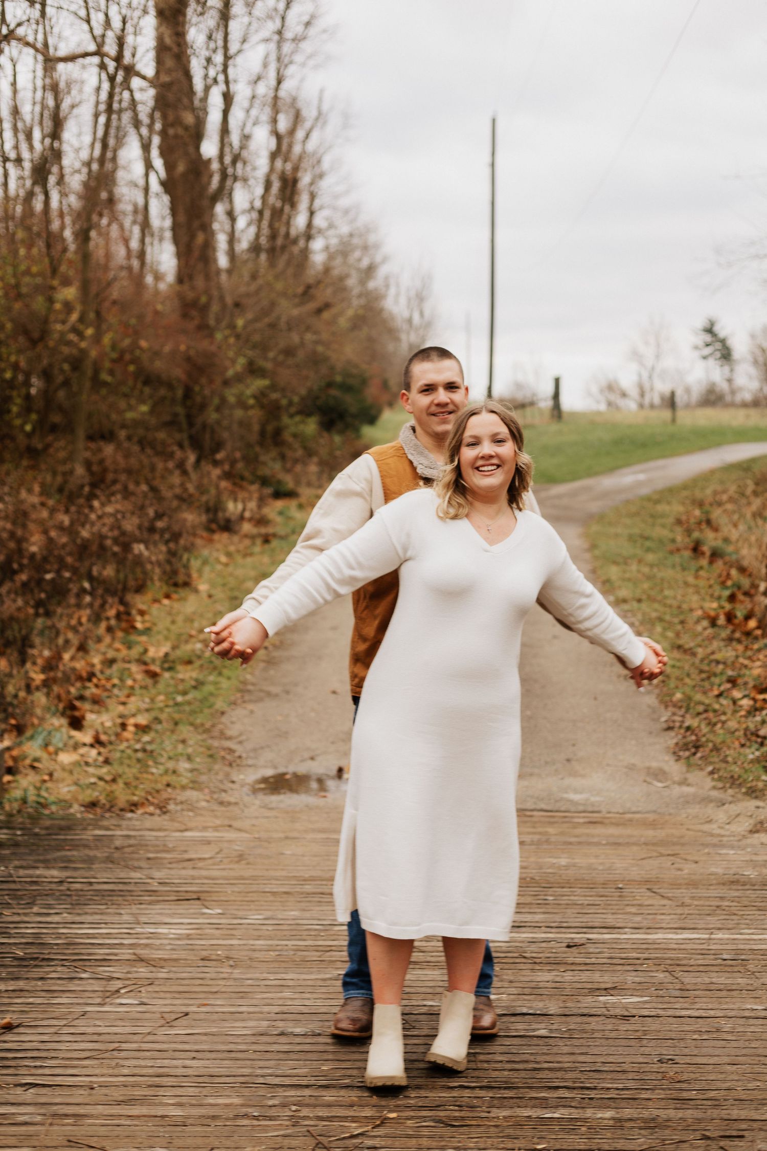 Couple in casual attire enjoying playful moment on wooden boardwalk in natural setting.