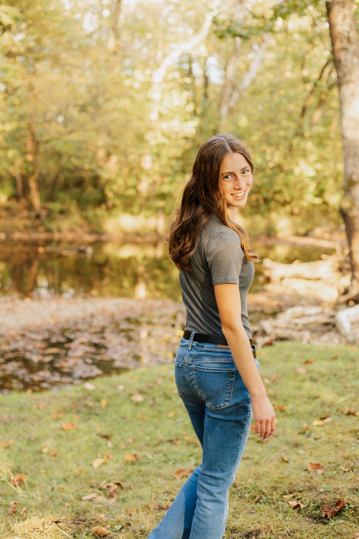 A casual outdoor photoshoot in a wooded setting with natural lighting and fallen leaves.