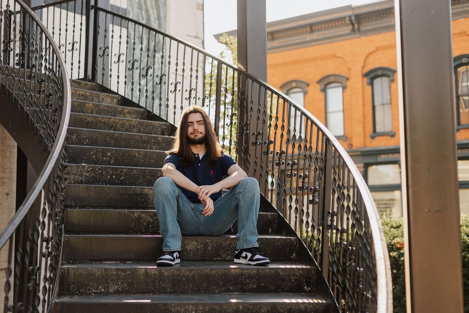 Person in casual attire sits on curved outdoor staircase with iron railings.