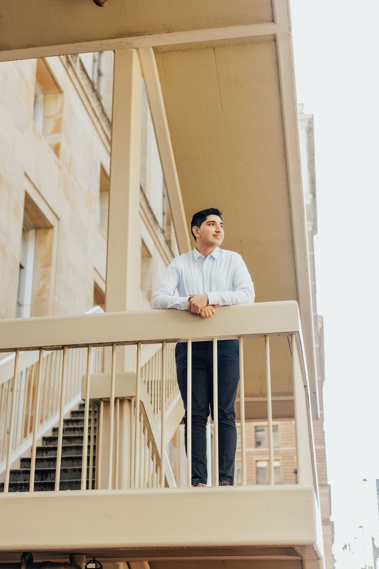Person in light blue shirt standing on beige apartment building balcony.