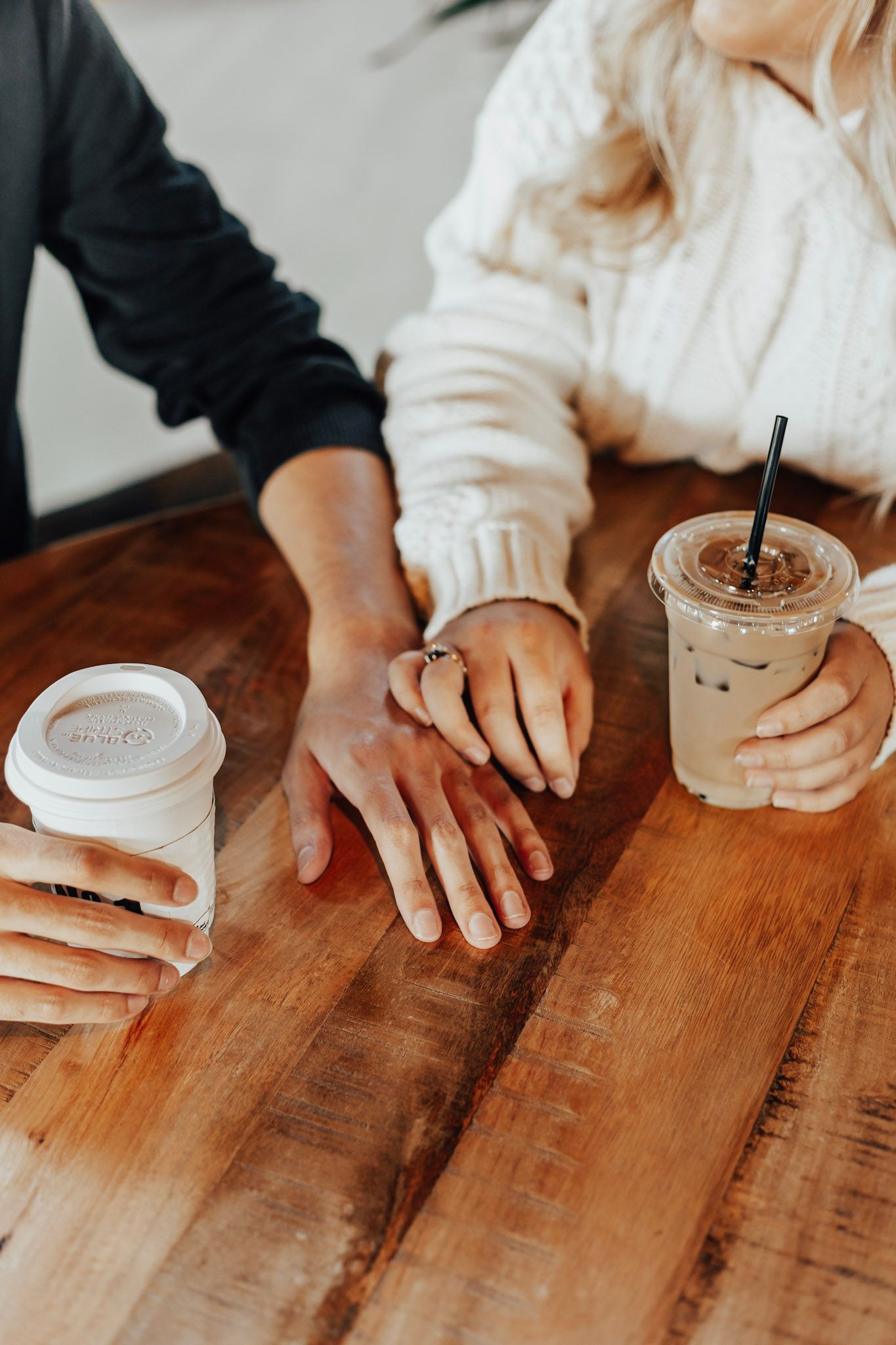 Hands placing coffee cups on rustic wooden table surface.