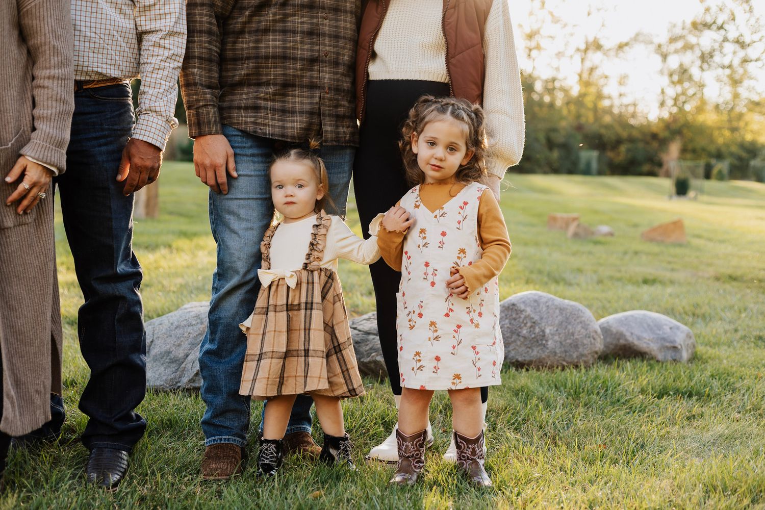Family members in coordinated casual outfits standing together on grass during sunset.