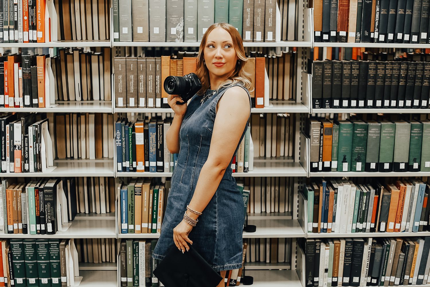 Photographer in denim outfit standing among library bookshelves.