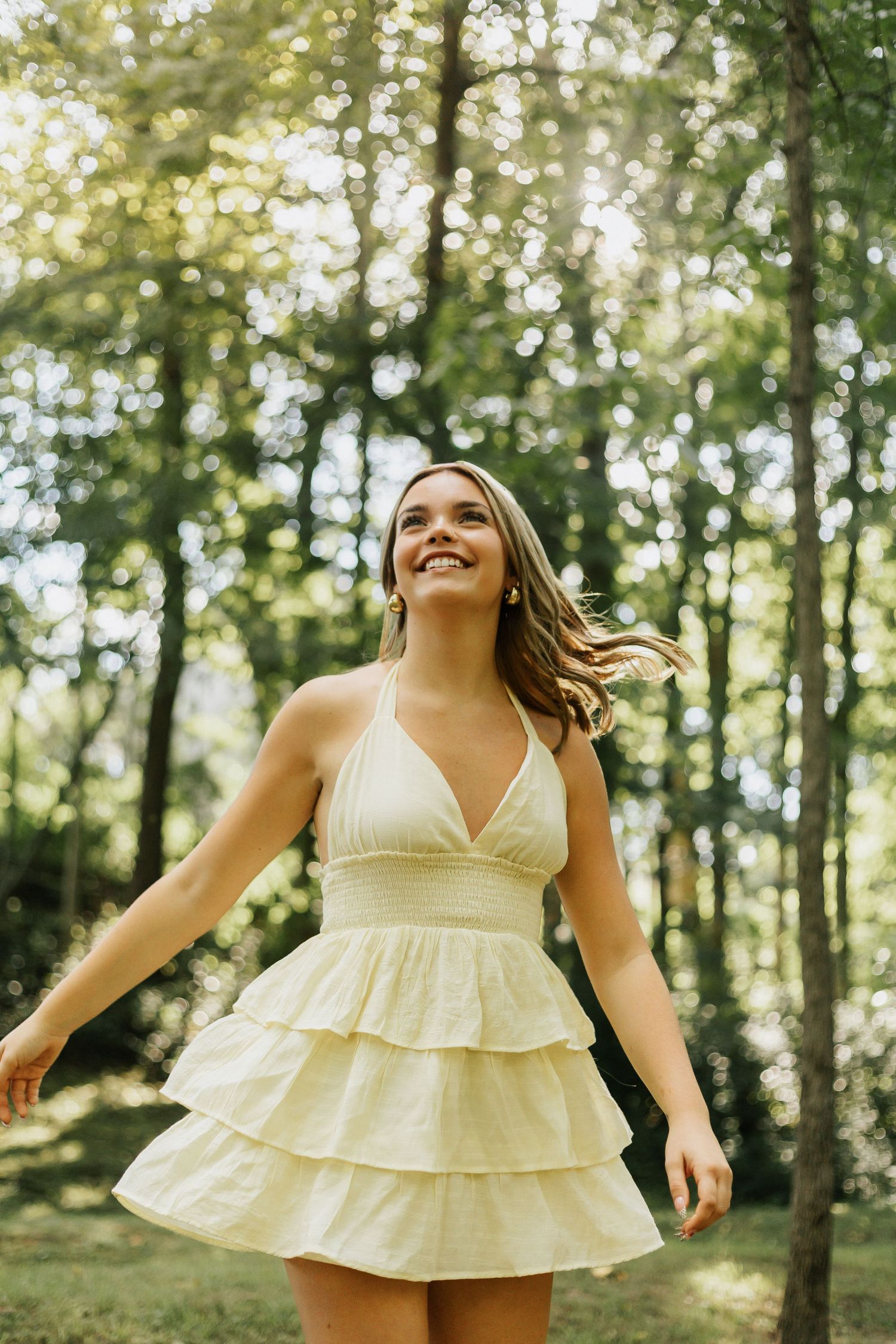 A playful outdoor photoshoot featuring a ruffled cream sundress in a sun-lit forest.
