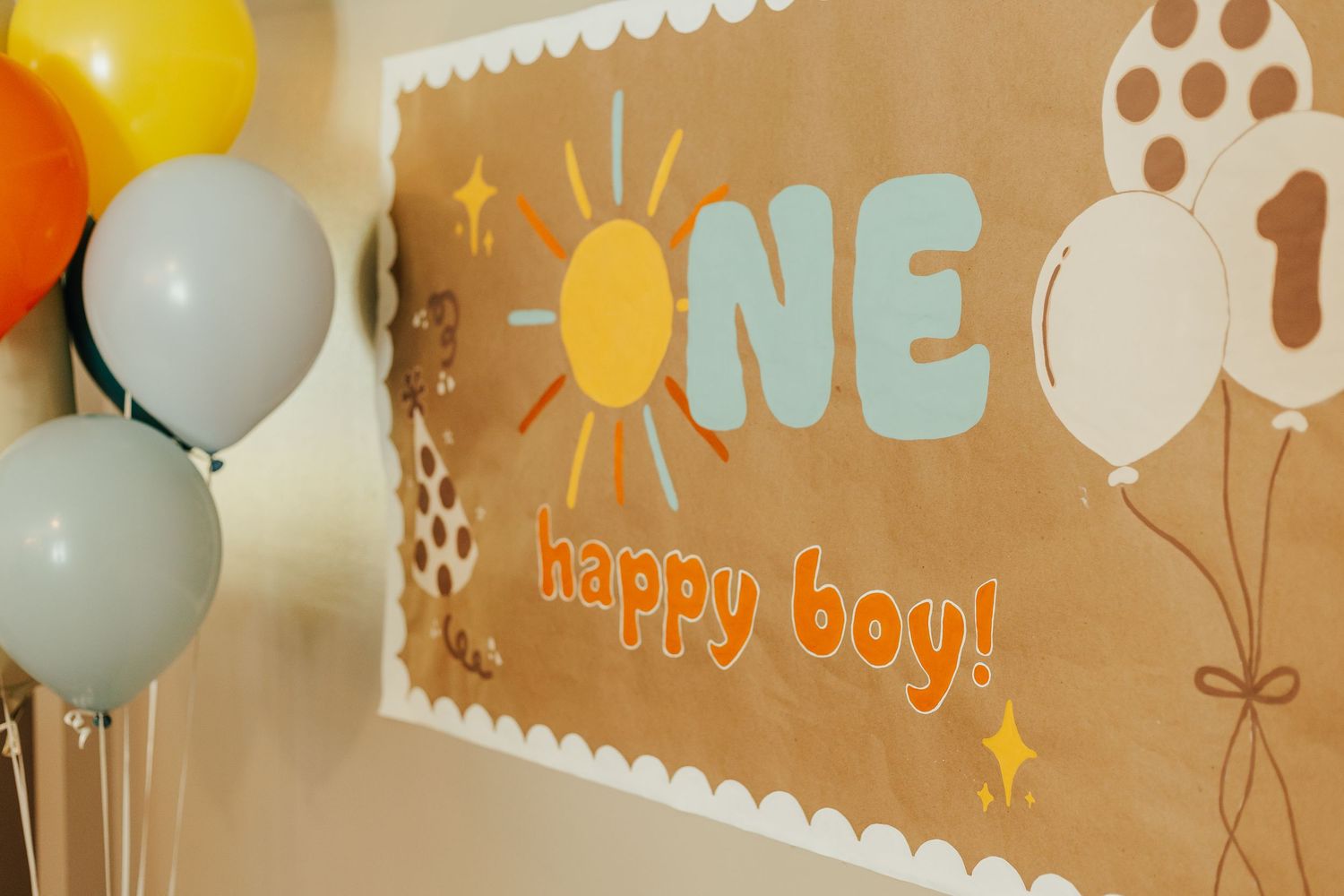 Brown and orange birthday party decorations with balloons against wall.