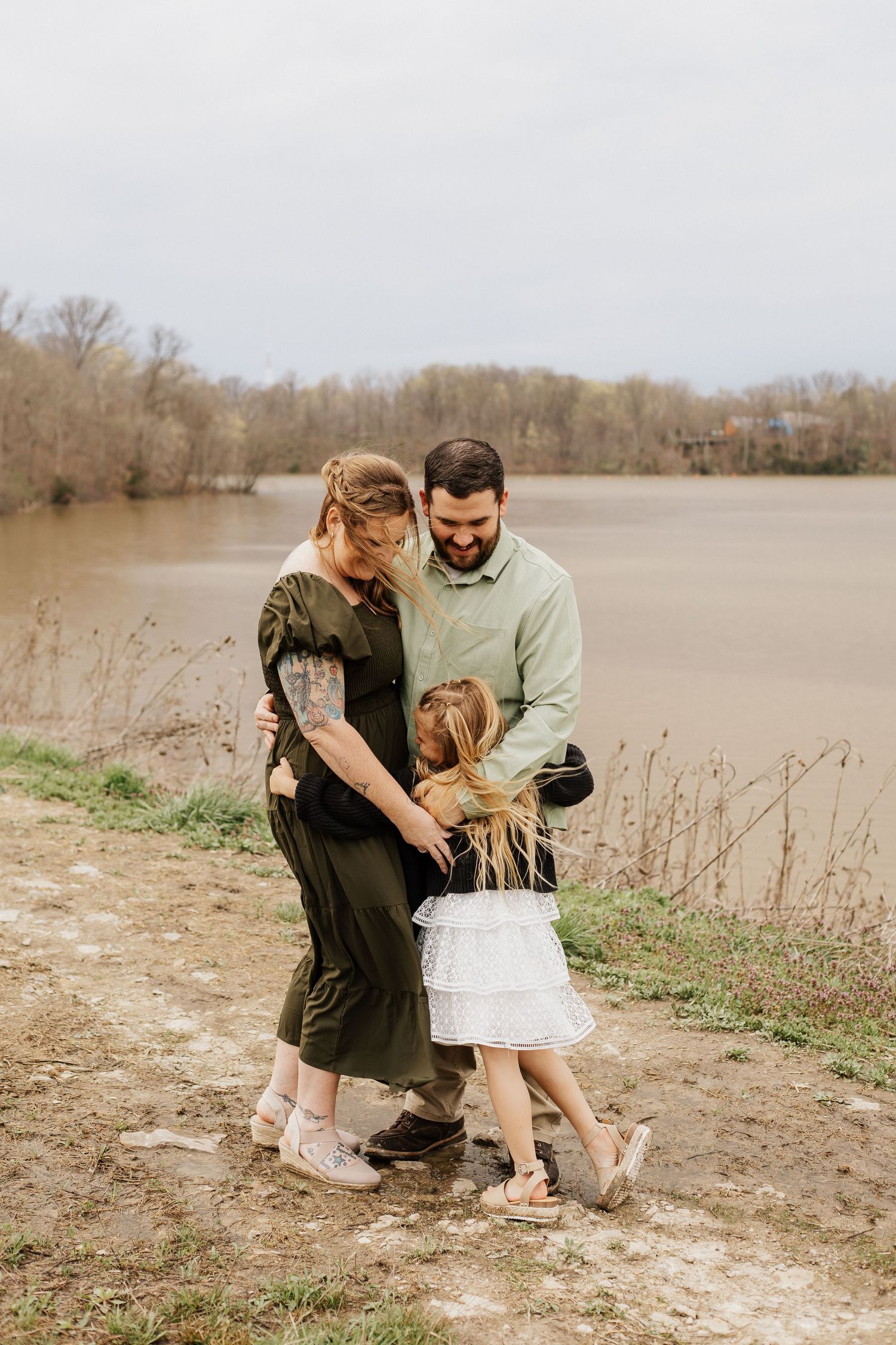 Family having outdoor photo session near lake with bare trees in background.