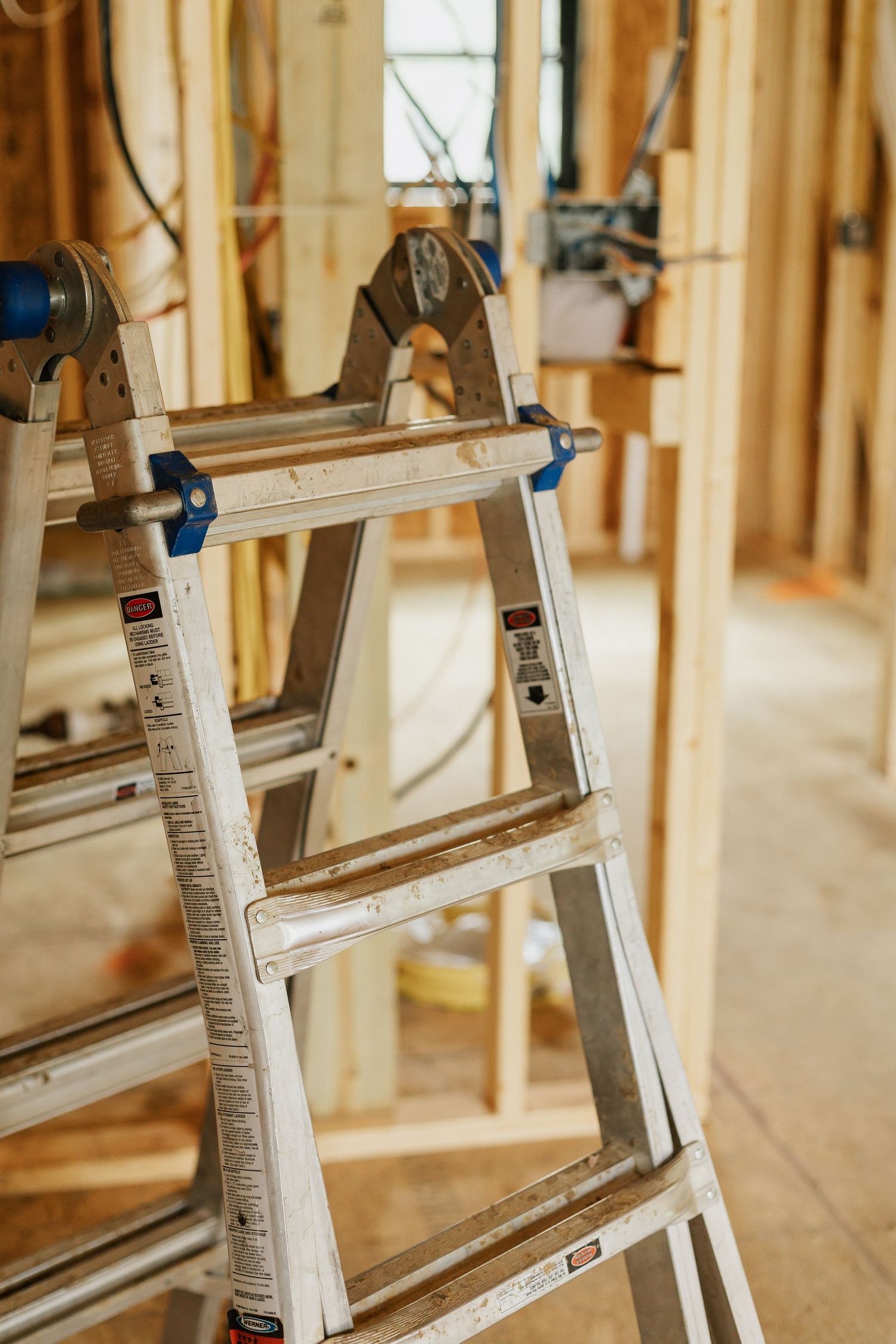Multiple aluminum ladders lined up against wooden framing in construction site.