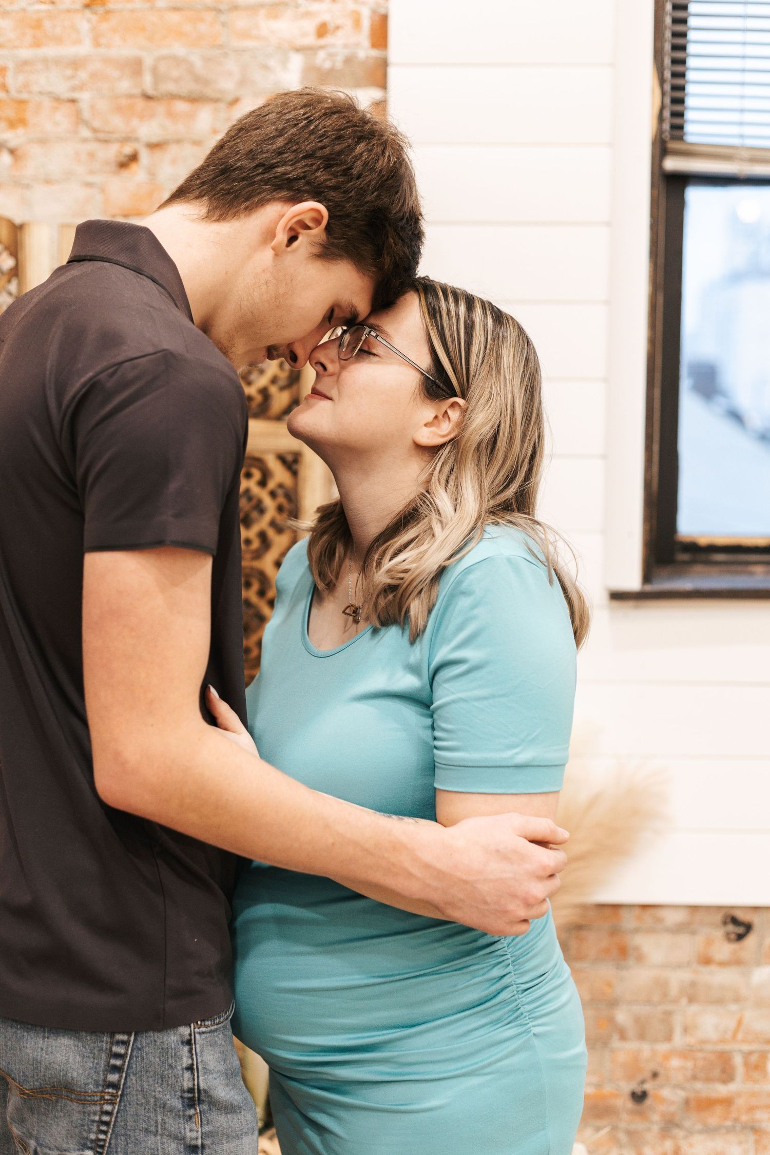 Intimate moments captured between couple with exposed brick wall and natural lighting.