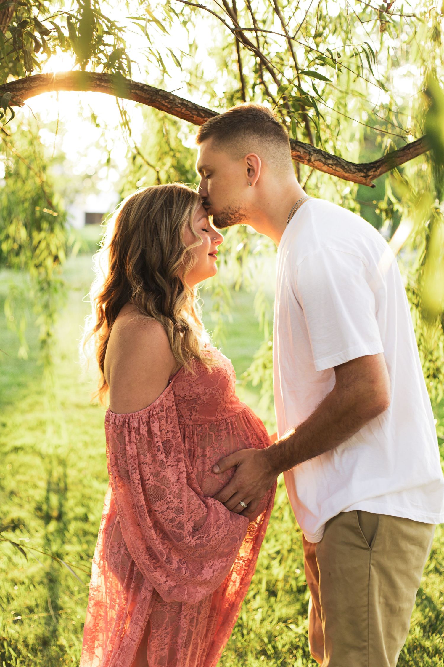 A romantic maternity photoshoot under willow trees at golden hour.