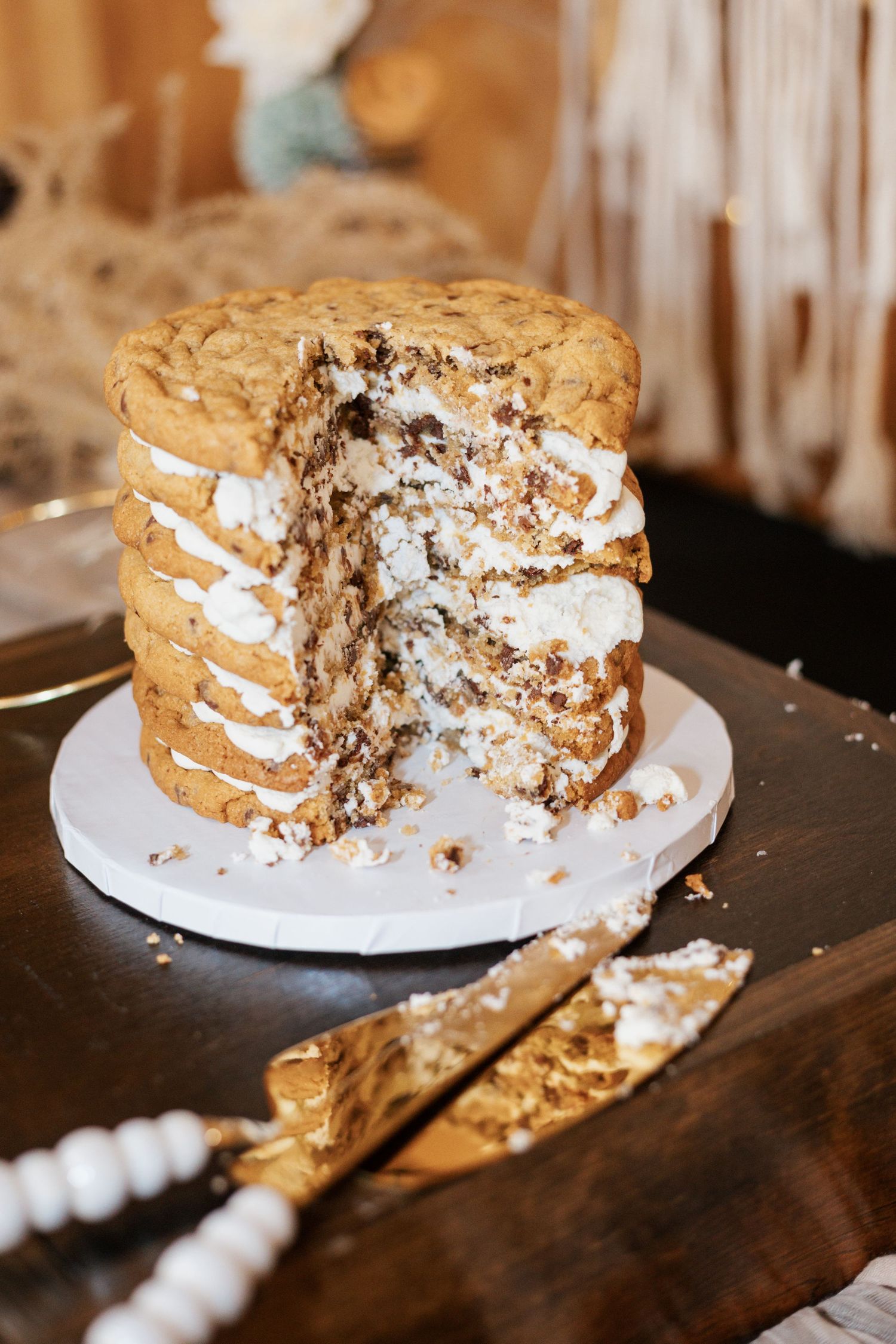 A layered cream-filled cake with crumbs scattered on a wooden surface shows progressive slices being removed.