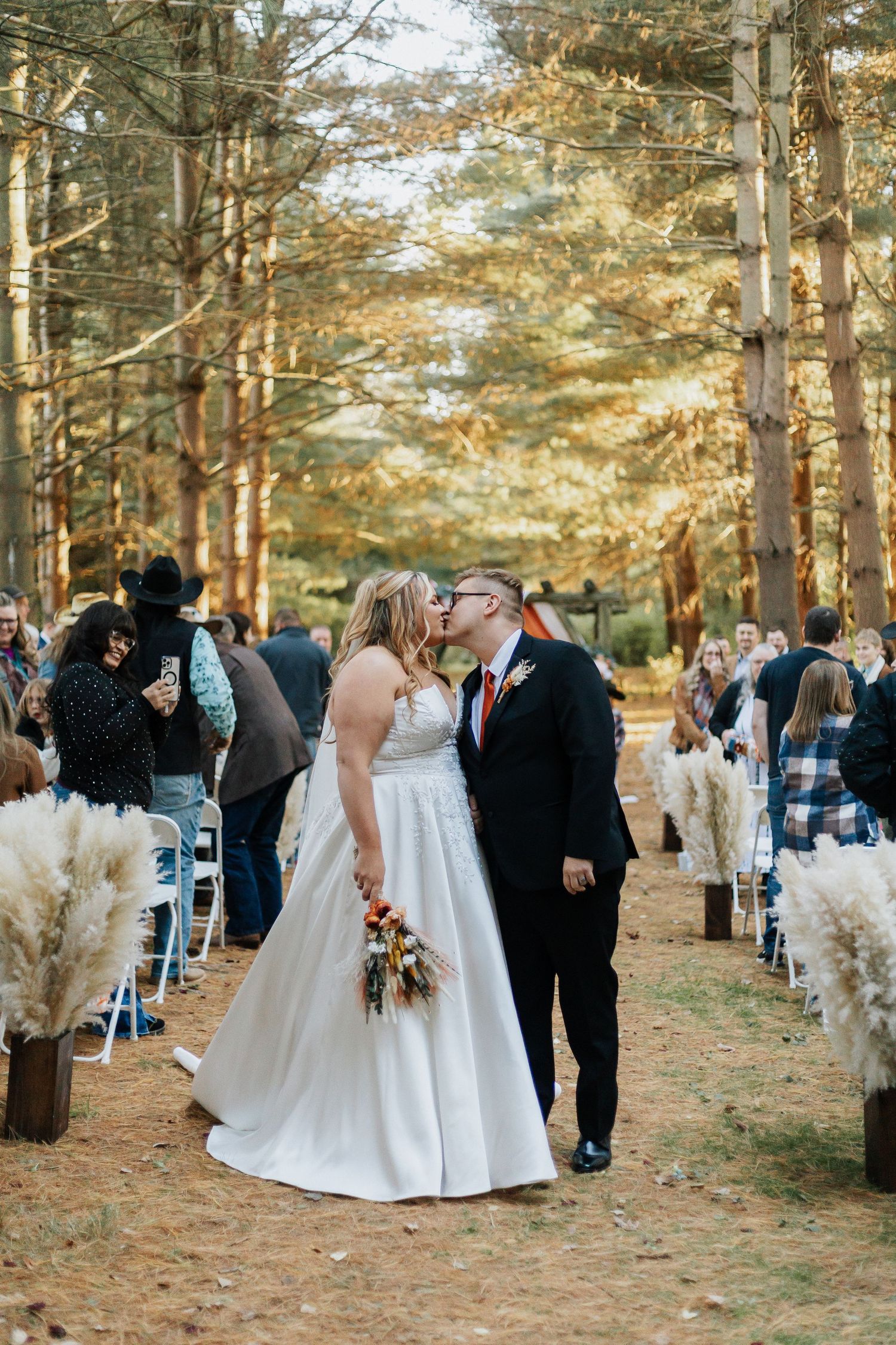 Outdoor forest wedding ceremony with white chairs and pampas grass decorations.