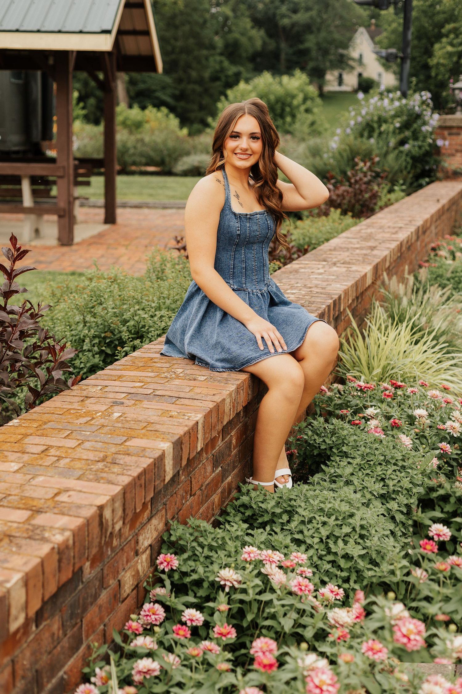 Summer portrait session on a brick wall surrounded by blooming pink flowers and greenery.