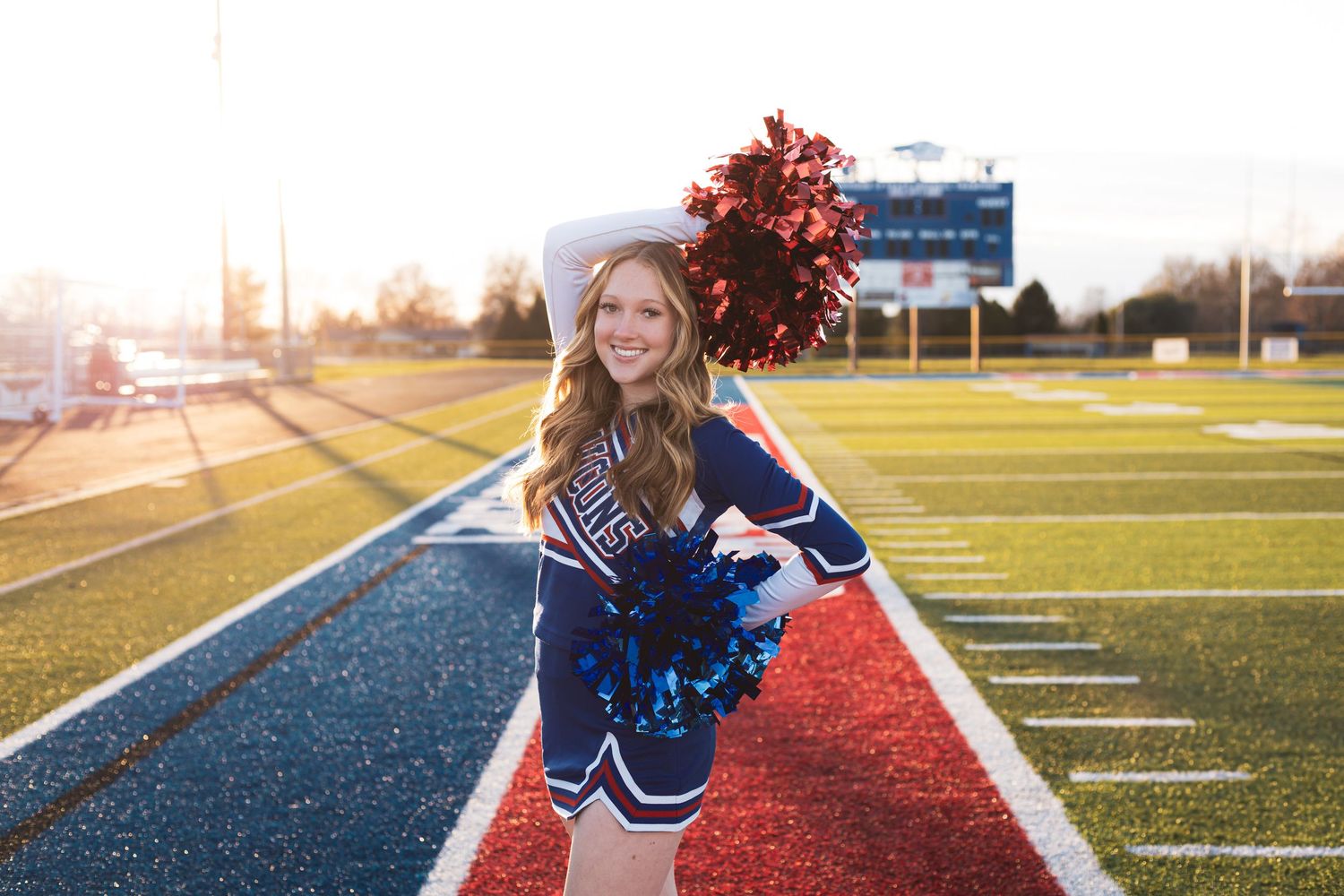 Sports field photoshoot with cheerleading props at golden hour.