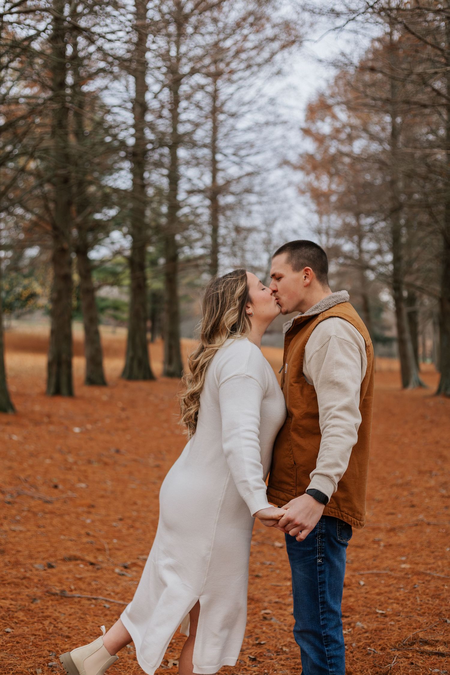 Romantic couple poses in a forest with orange fallen leaves during autumn.