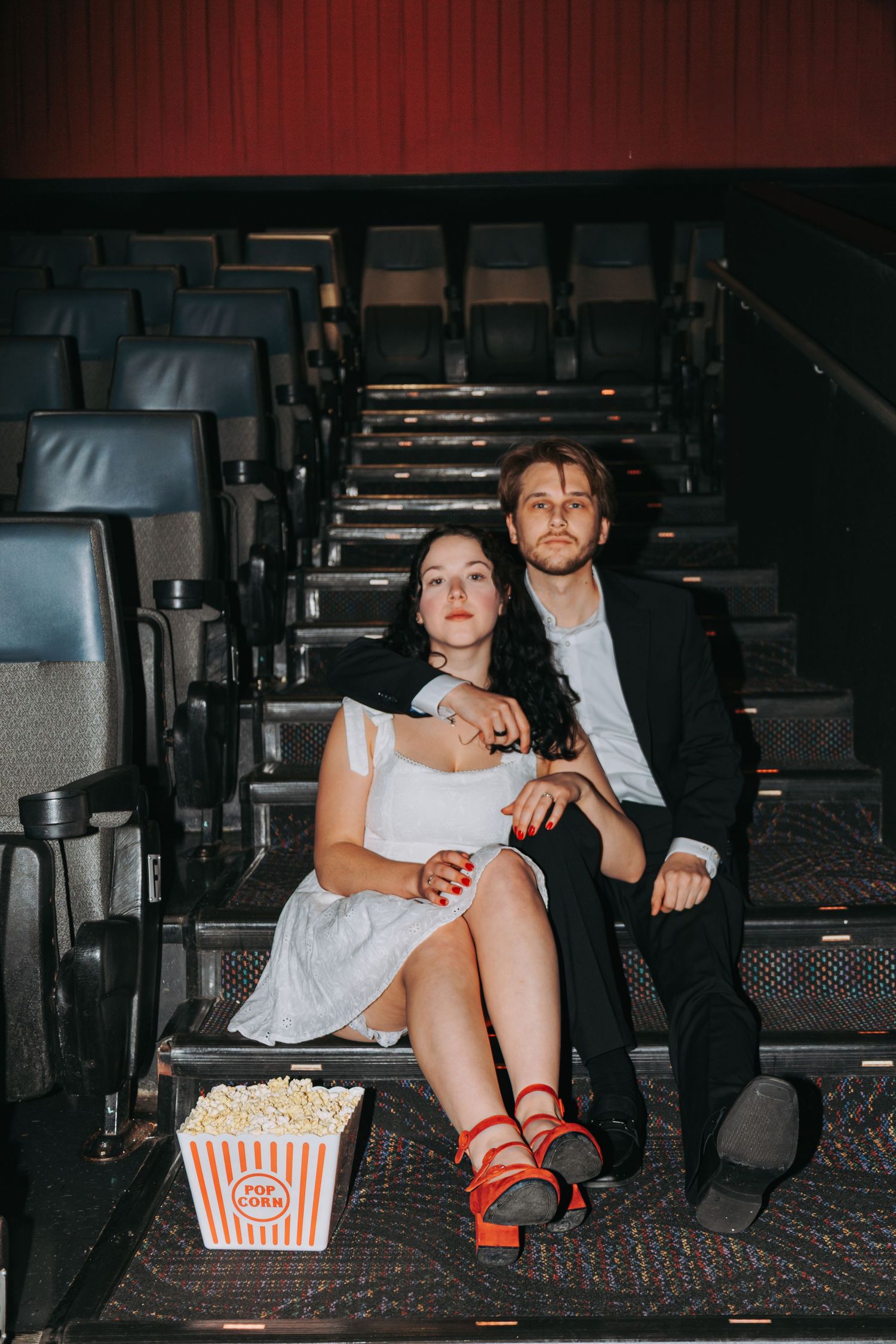 A movie theater scene with a popcorn bucket and red shoes visible in the dim lighting.