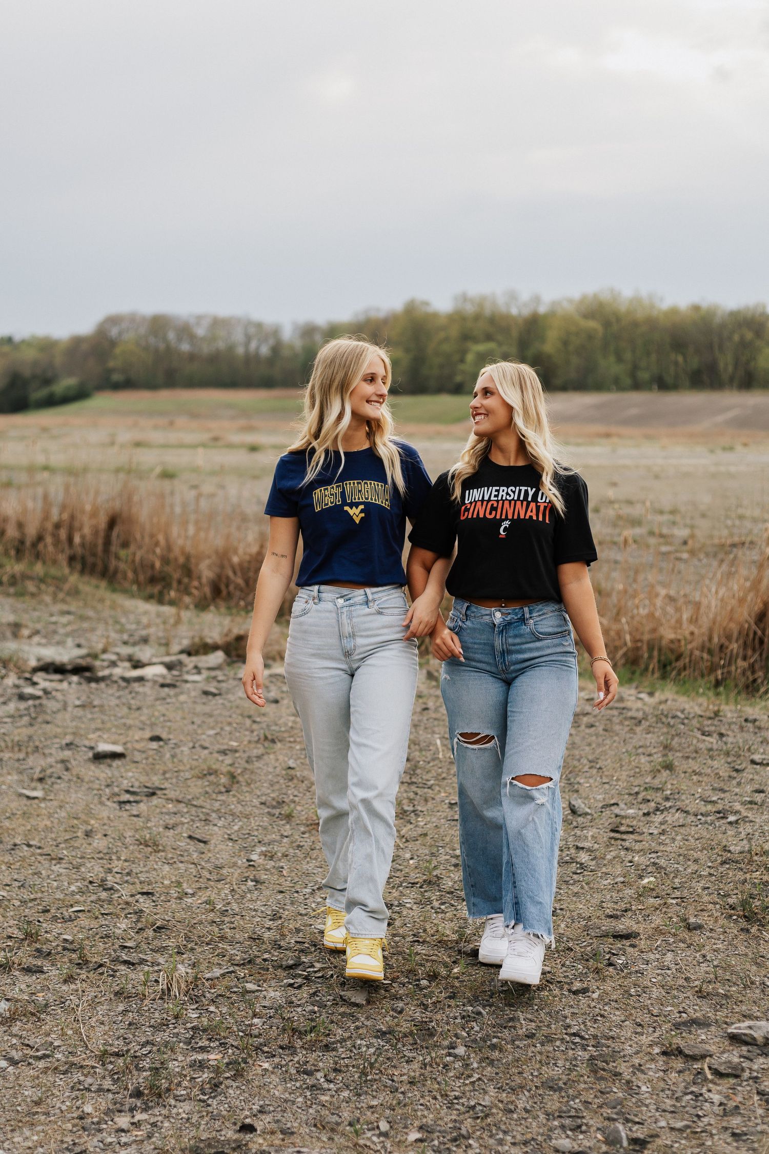 Two friends in matching jeans and t-shirts walking together in an open field.