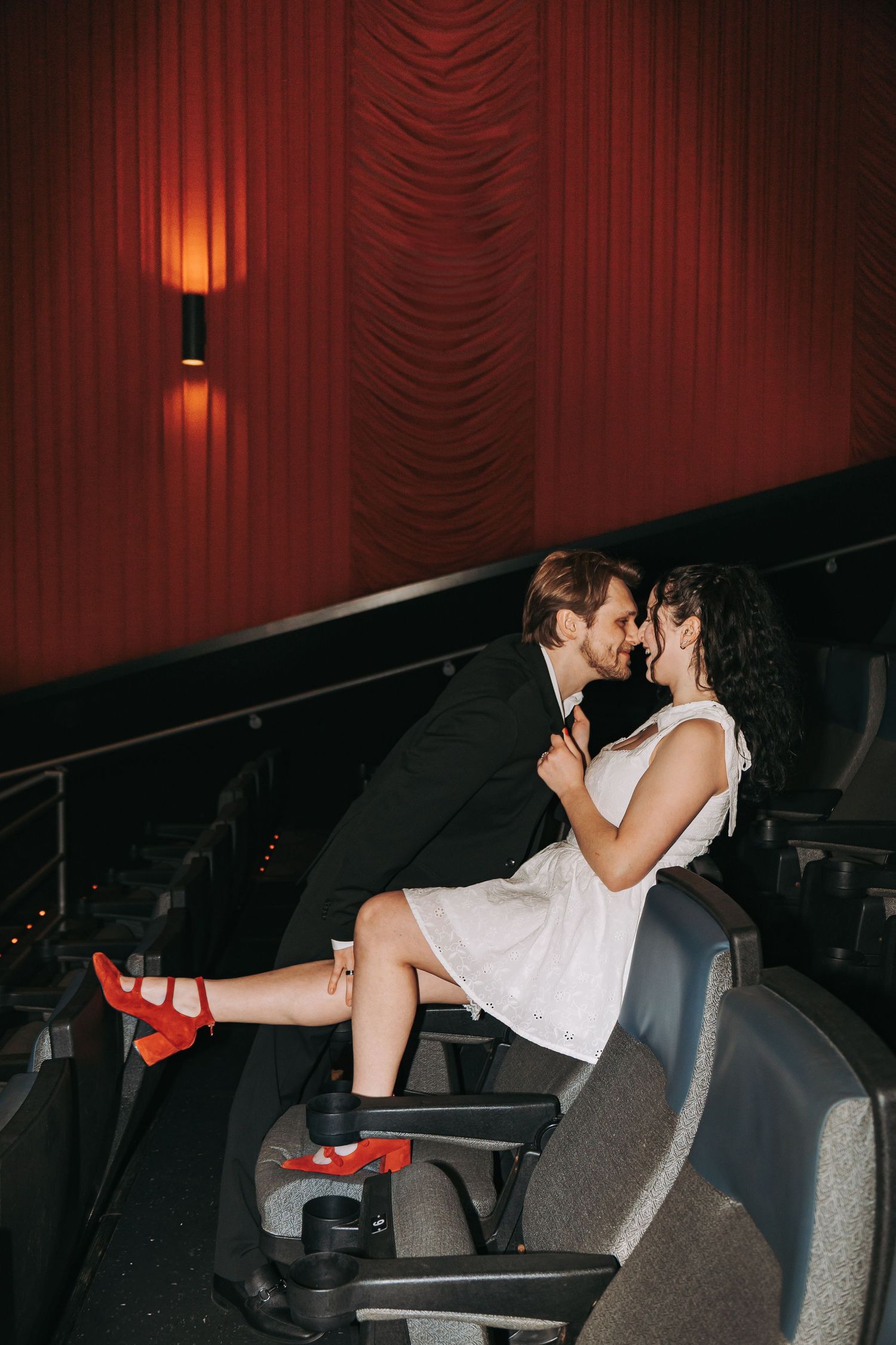 A dimly lit movie theater with red curtains and plush seating.